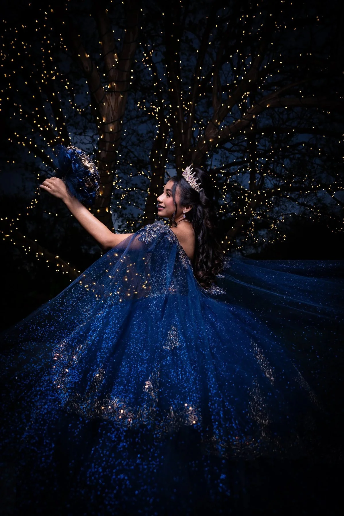 Quinceañera in navy-blue glitter gown twirling under fairy-light trees at a DFW preshoot