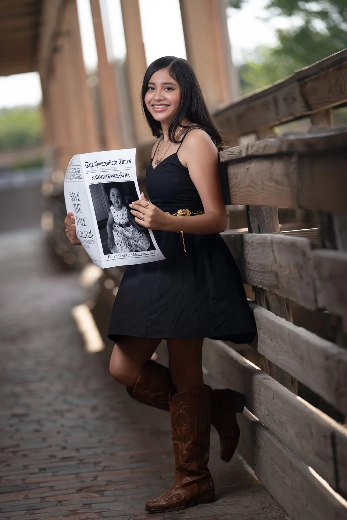 Quinceañera holding a Save the Date newspaper on a covered bridge in Fort Worth