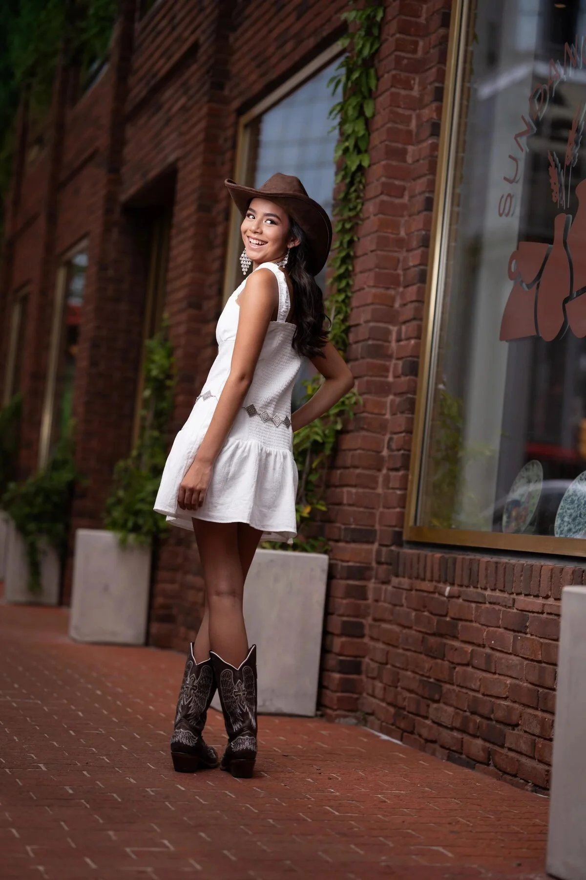 Quinceañera in a white western dress and cowboy hat by a downtown Fort Worth storefront