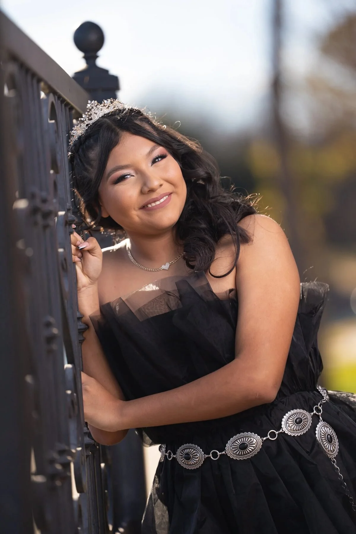 Quinceañera in a black tulle dress and concho belt by an iron gate in Texas