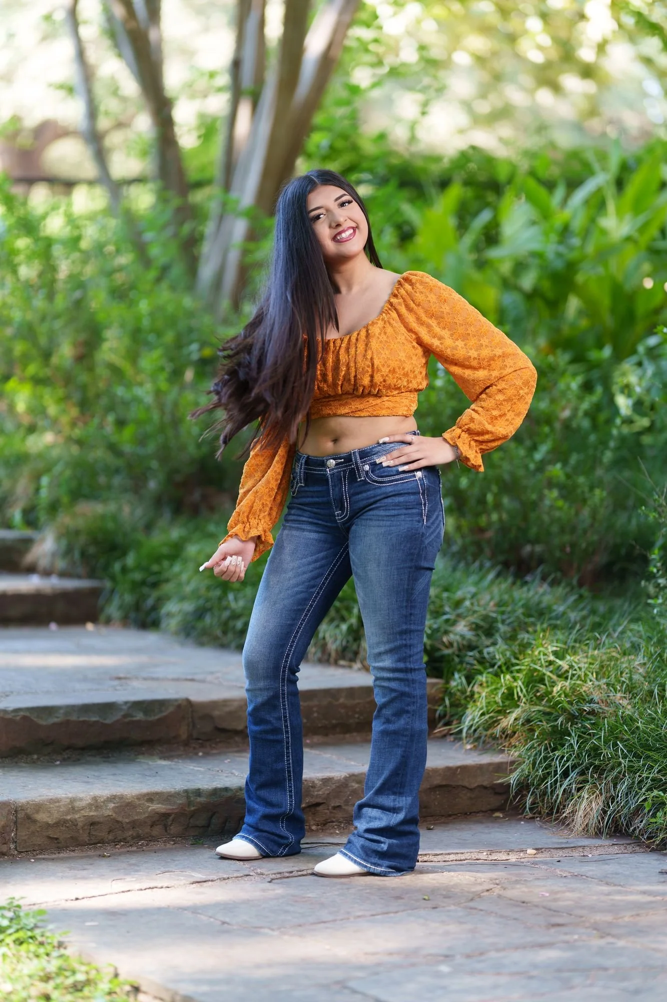Nevaeh mid-laugh on a garden pathway at Fort Worth Botanic Garden with her hair in motion during her boho western Save the Date