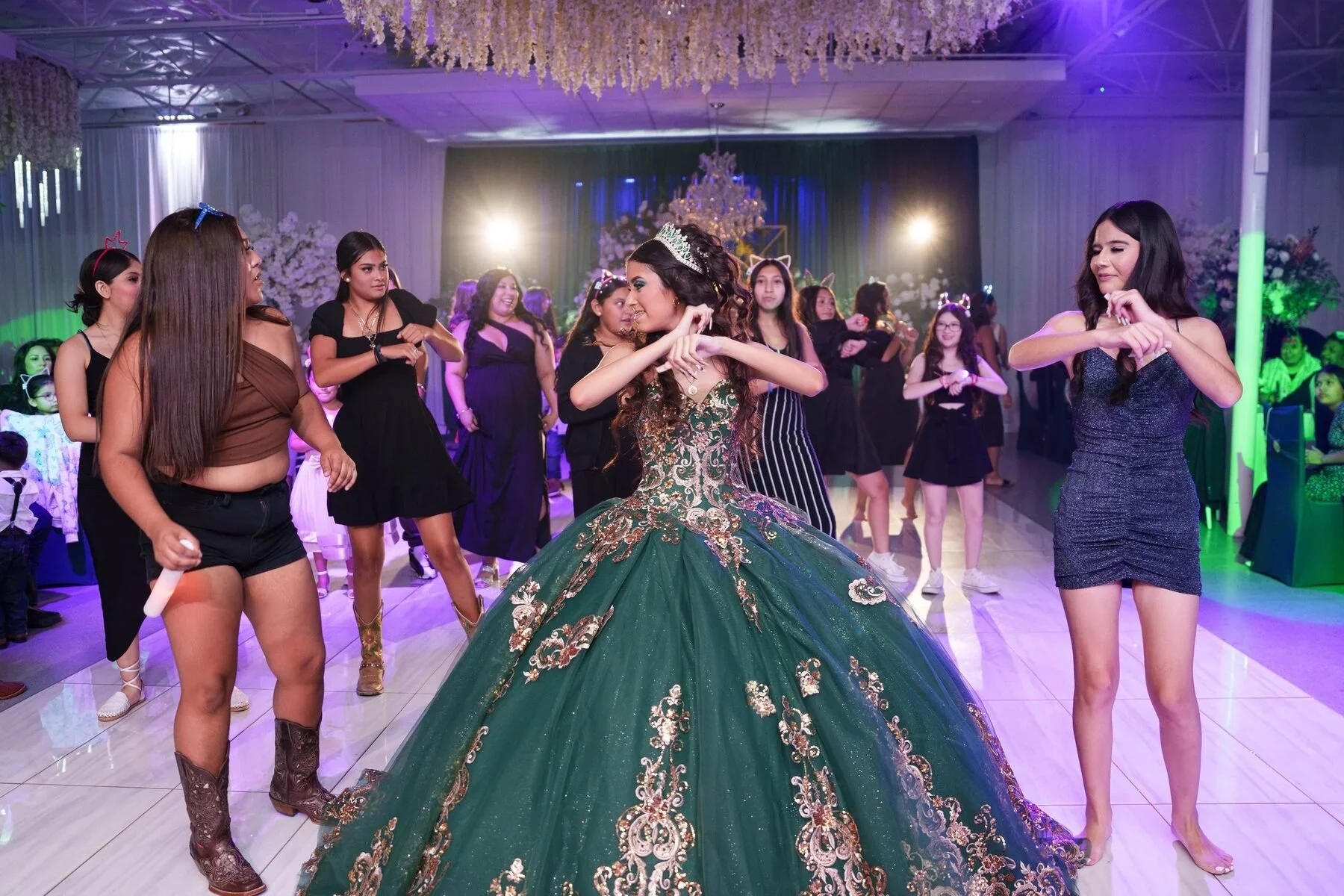 Quinceañera in an emerald and gold gown dancing with friends at a DFW reception