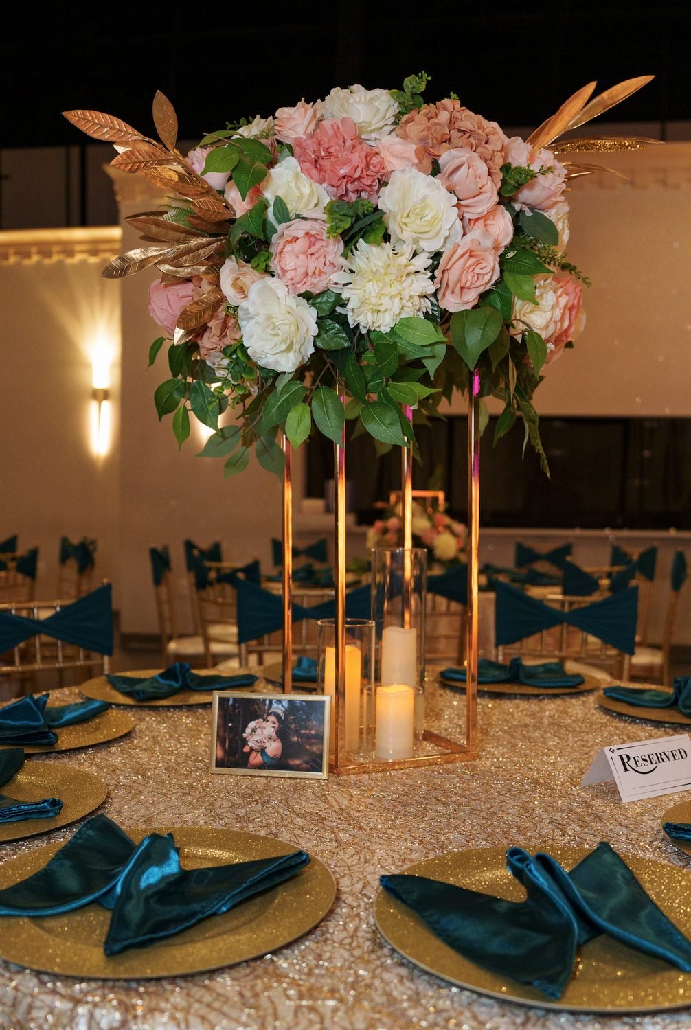 Centro de mesa alto de quinceañera con rosas rosadas y follaje sobre mesa con lentejuelas y servilletas de terciopelo