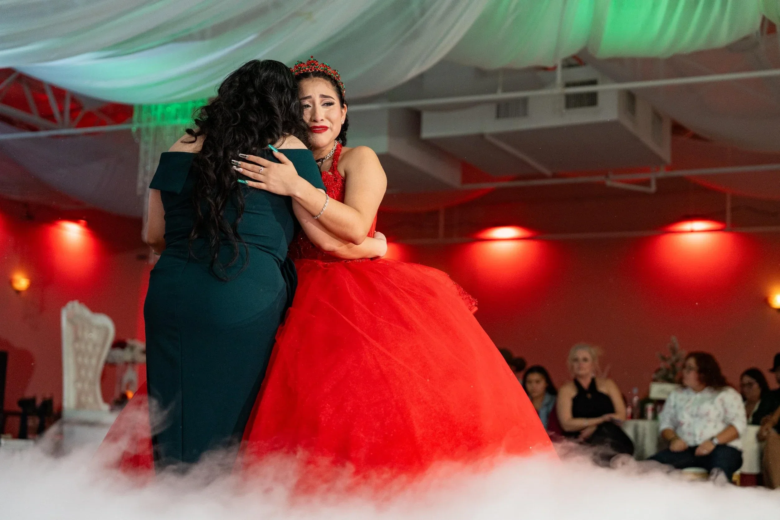 Quinceanera in a red gown embraces her mother during a DFW celebration.