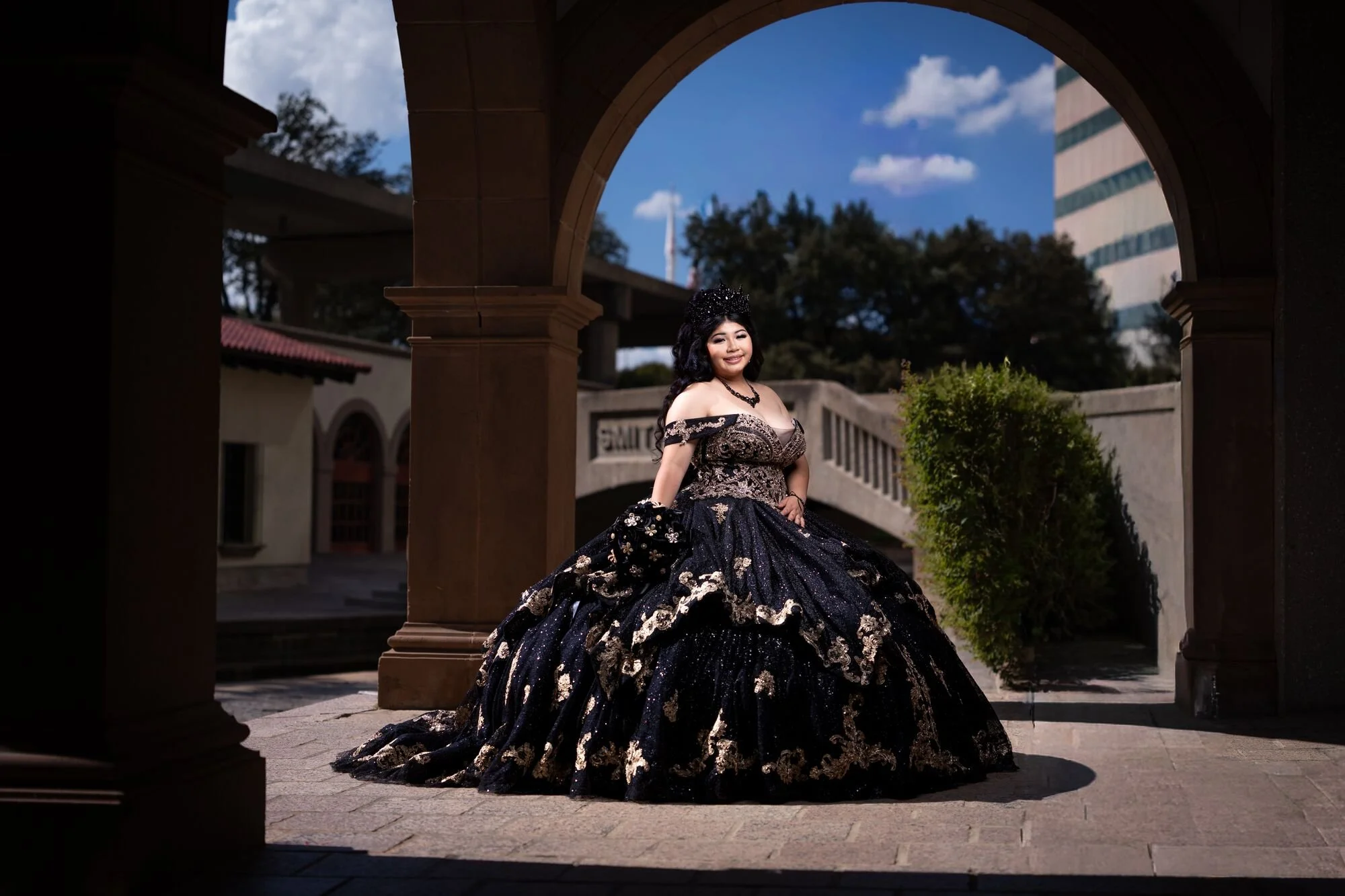 Black and gold quinceañera preshoot under archway at Mandalay Canal Las Colinas Irving TX with skyline backdrop