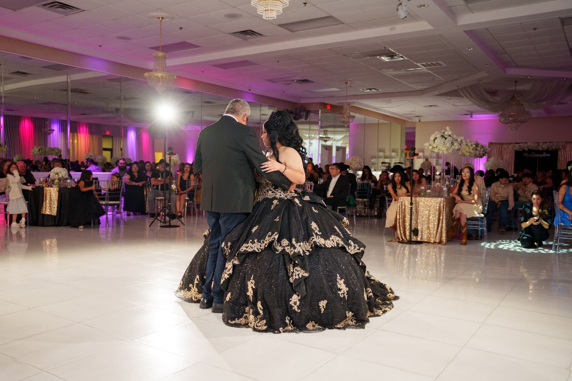 Jayden in black and gold quinceañera ballgown dancing with her grandfather on the white dance floor at Luxor Banquet Hall Carrollton with family and guests watching