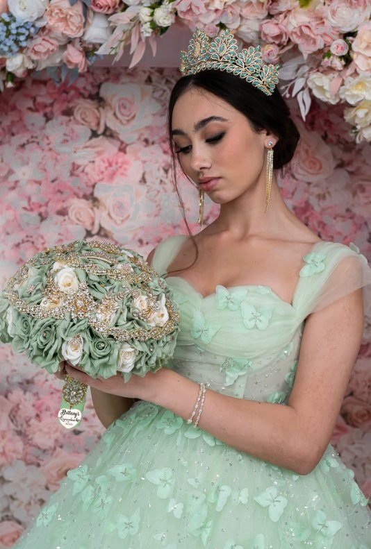 Quinceañera con vestido verde menta y corona sosteniendo un ramo floral