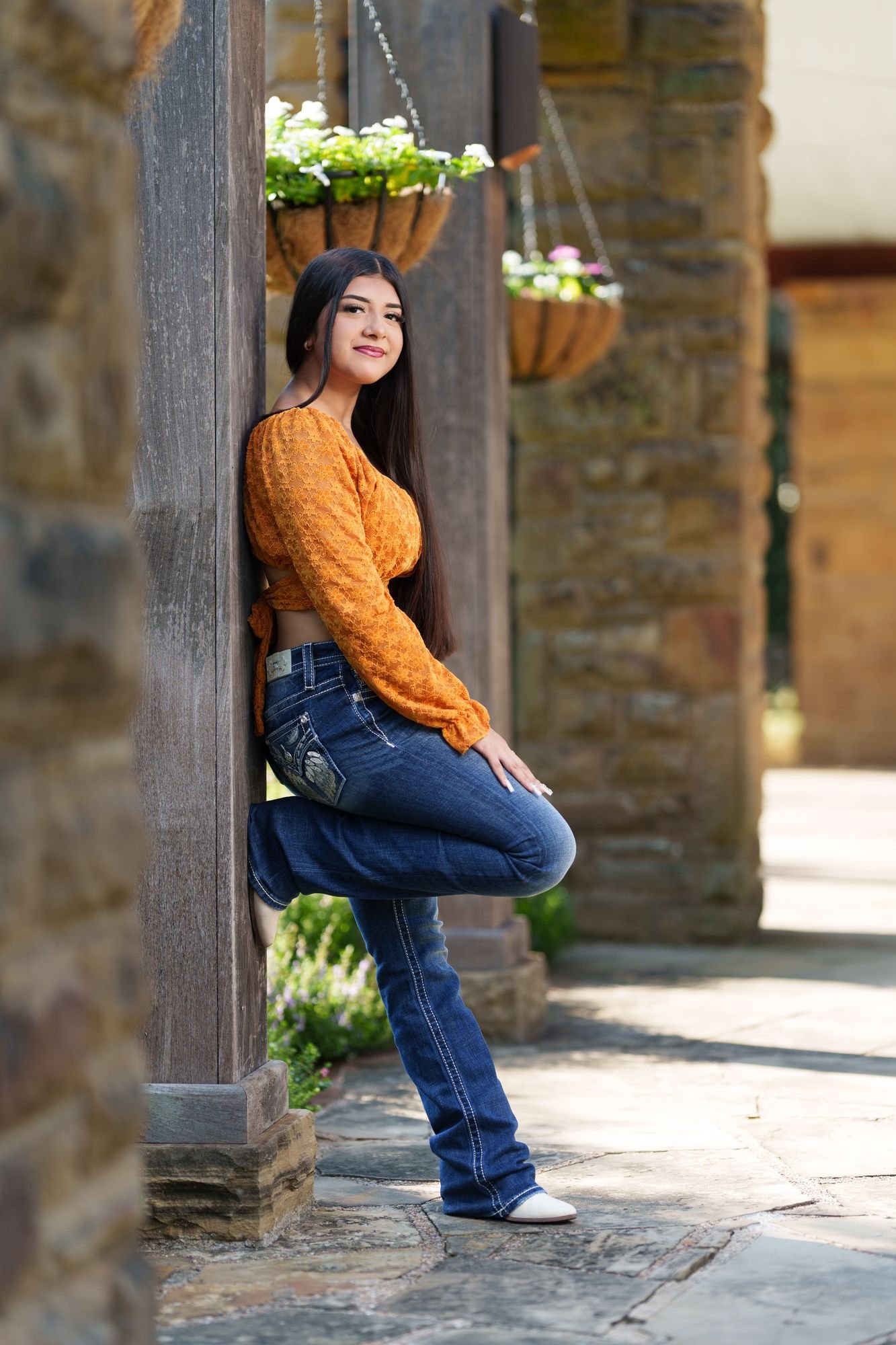 Nevaeh leaning against a stone pillar with hanging flower baskets at Fort Worth Botanic Garden during her boho western Save the Date