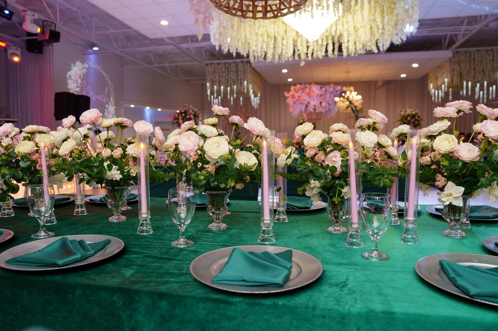 Reception dining room at Blanc Event Center with chandeliers, white and pink floral centerpieces, and emerald green linens