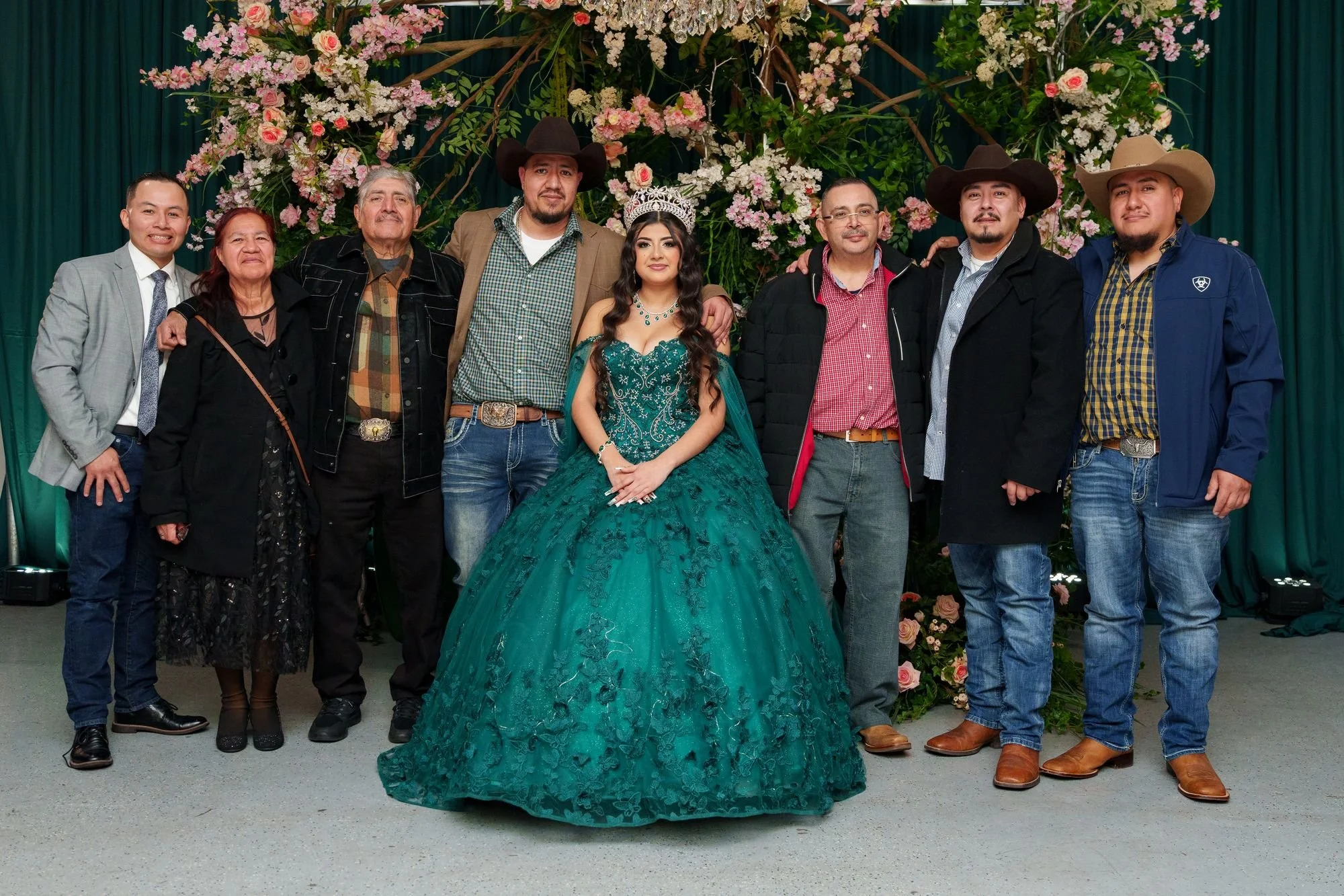 Nevaeh with her extended family in her emerald quinceañera ballgown at Blanc Event Center Dallas, with cowboy hats and a floral arch backdrop — a Texas quinceañera family portrait