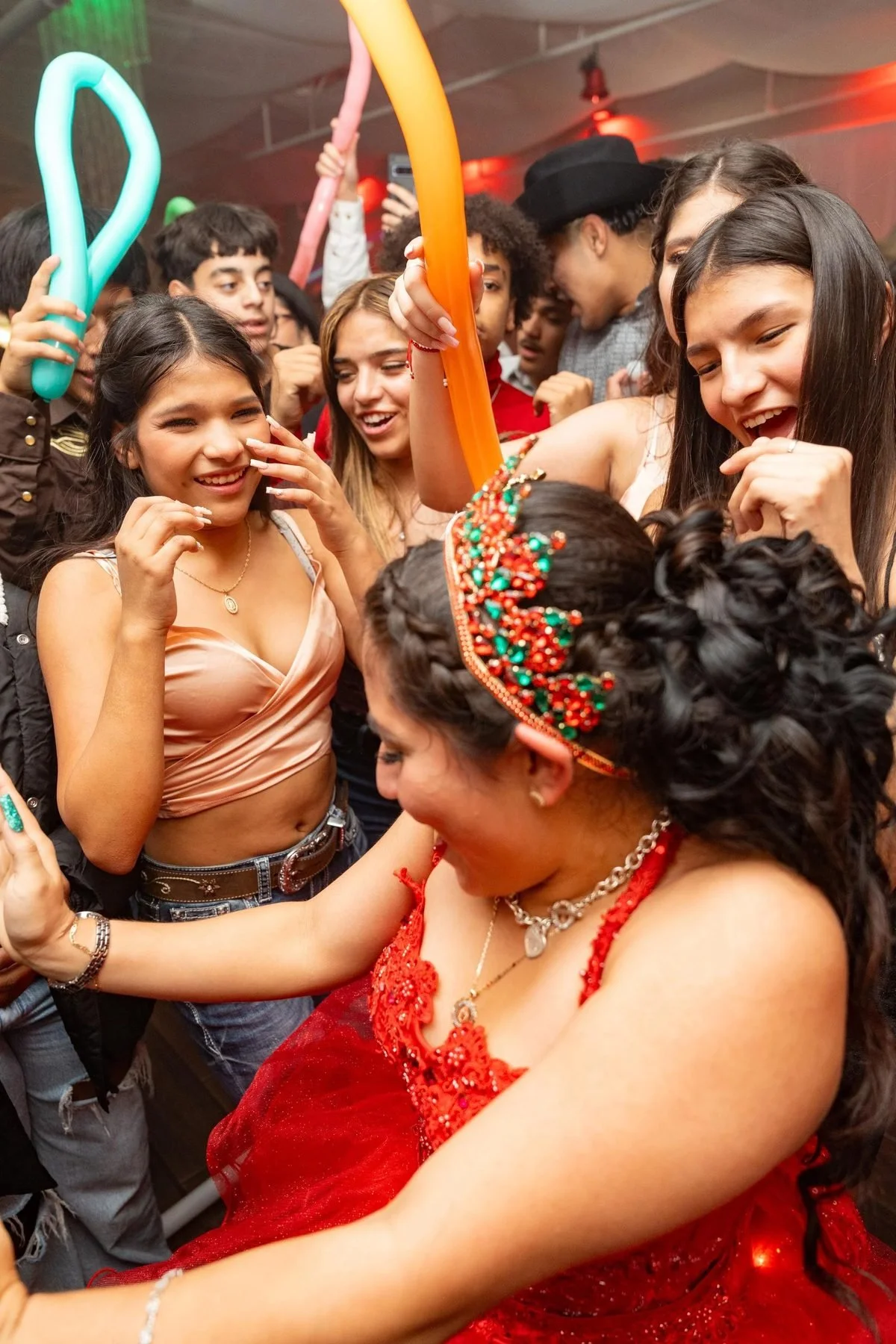 Quinceañera in red gown and crown laughing with friends on the dance floor during reception celebration