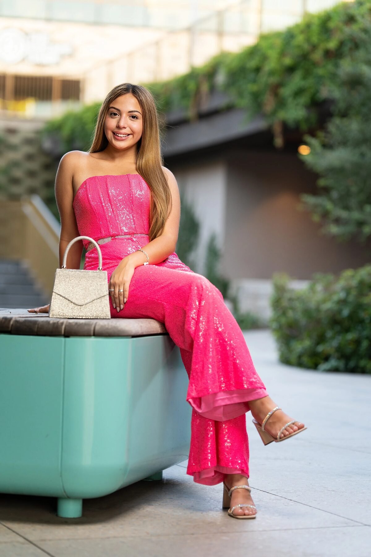 Teen in a hot pink jumpsuit on a teal bench during a DFW quinceañera shoot