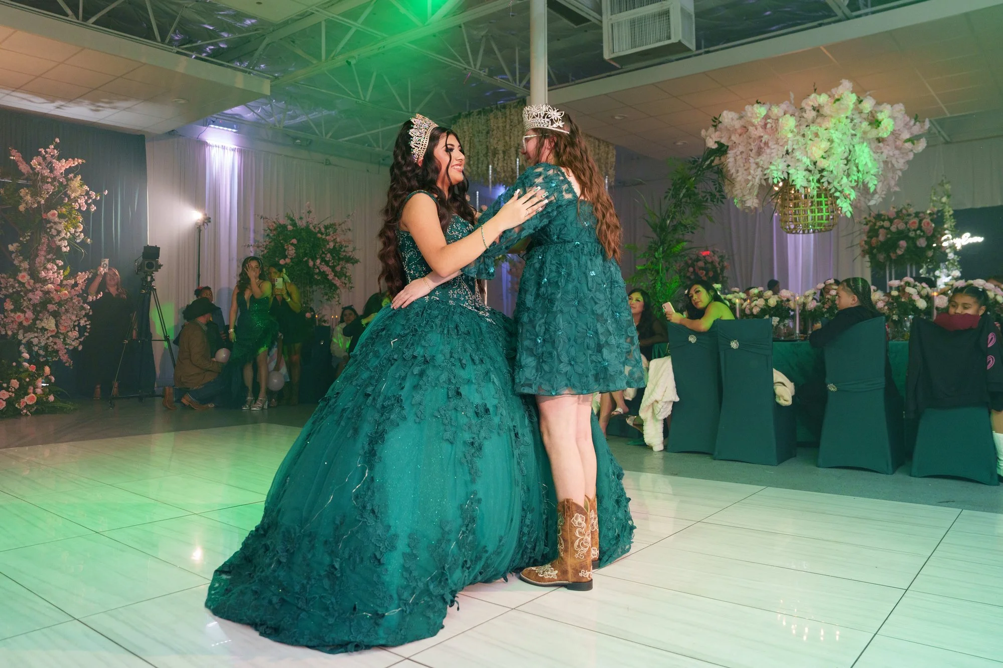 Nevaeh dancing with her younger sister on the dance floor, both wearing crowns, sister wearing western cowboy boots with her emerald dress