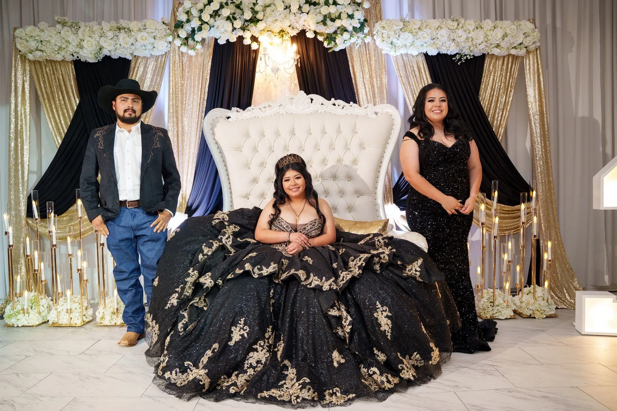 Quinceañera Jayden seated on white tufted throne with father in black suede Western jacket and mother in black sequin gown standing beside her at Luxor Banquet Hall Carrollton TX