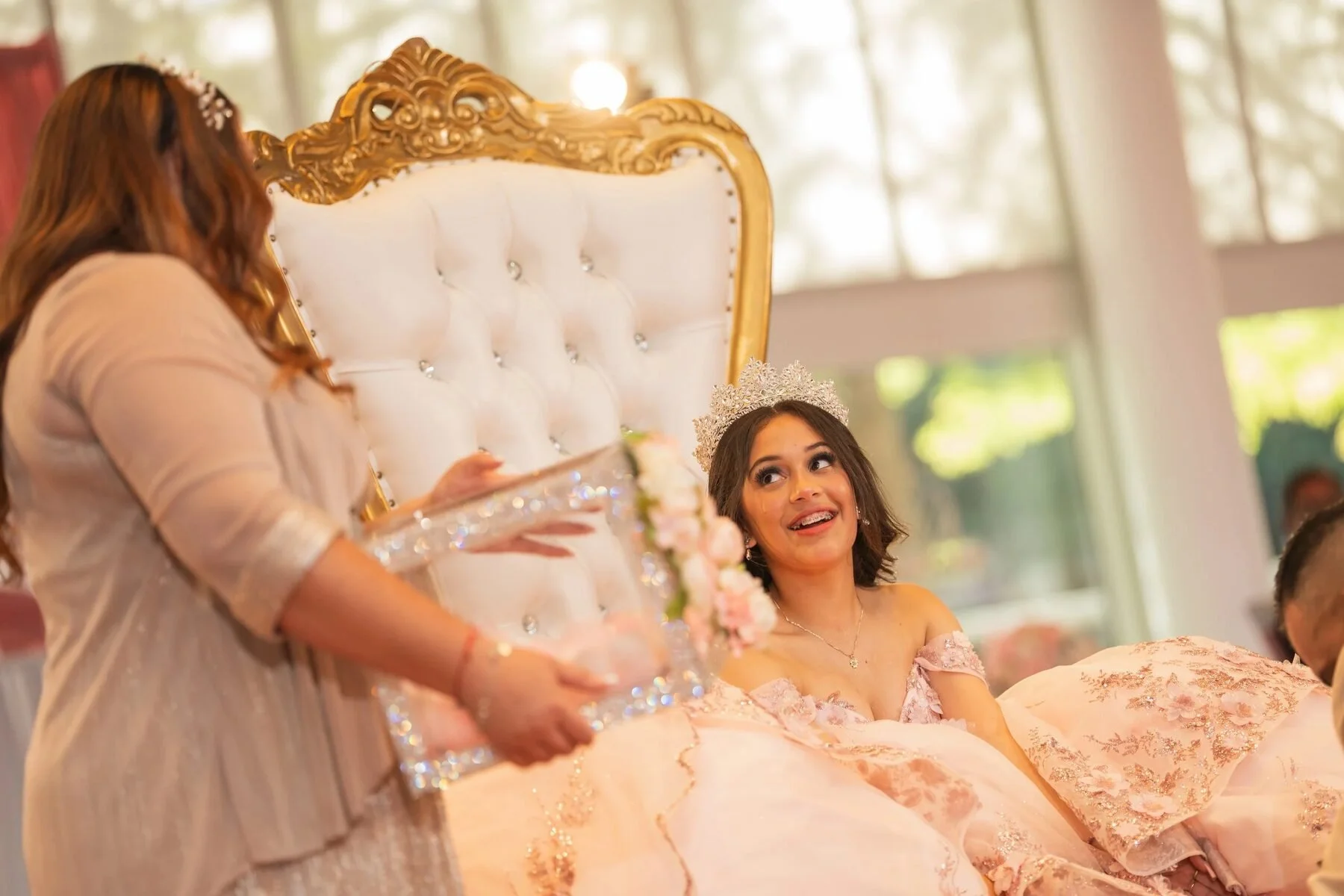 Quinceanera in a blush gown smiles from a gold throne chair at her Dallas reception.