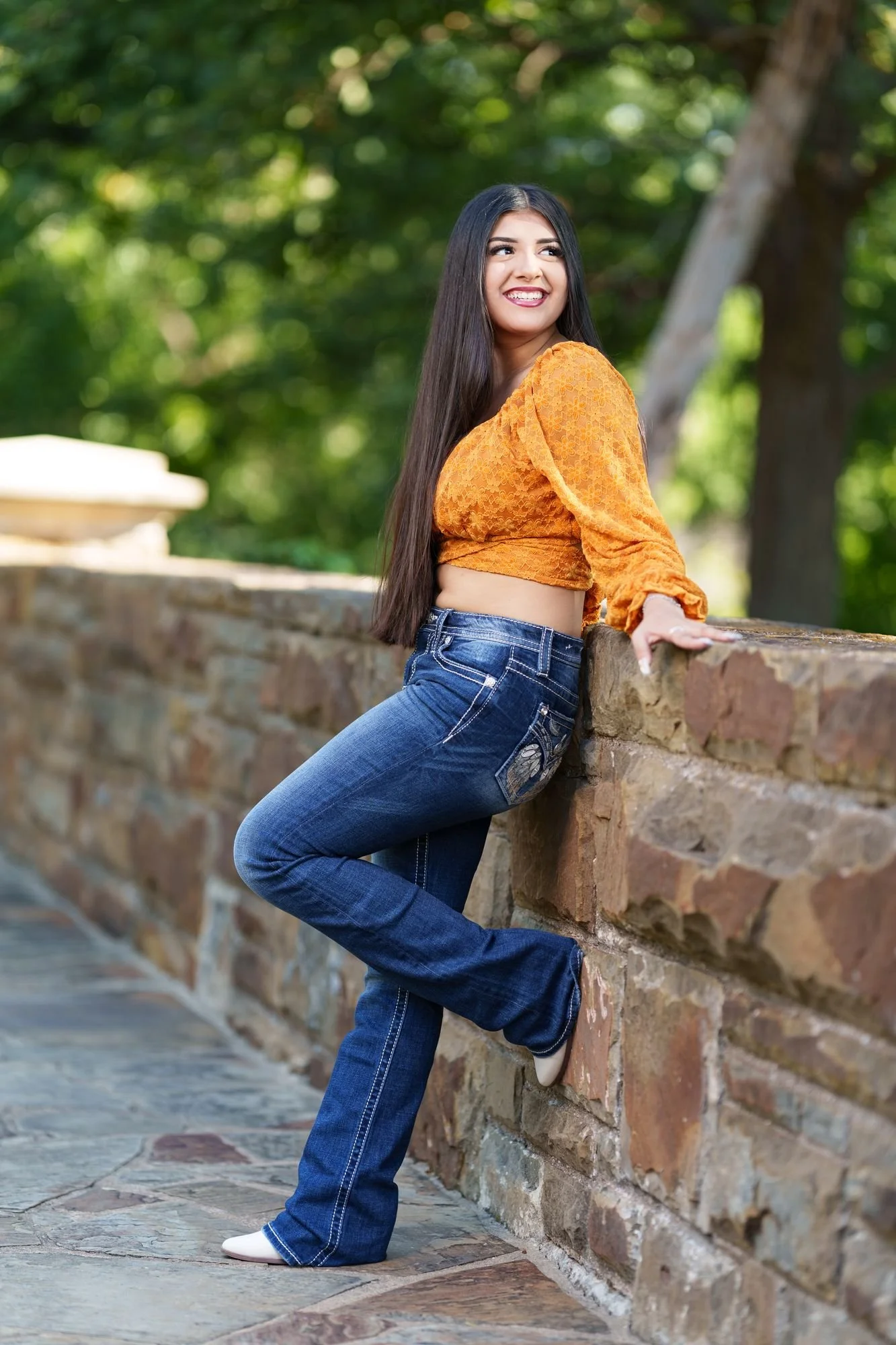Nevaeh leaning against a stone wall at Fort Worth Botanic Garden in her burnt orange boho western Save the Date outfit