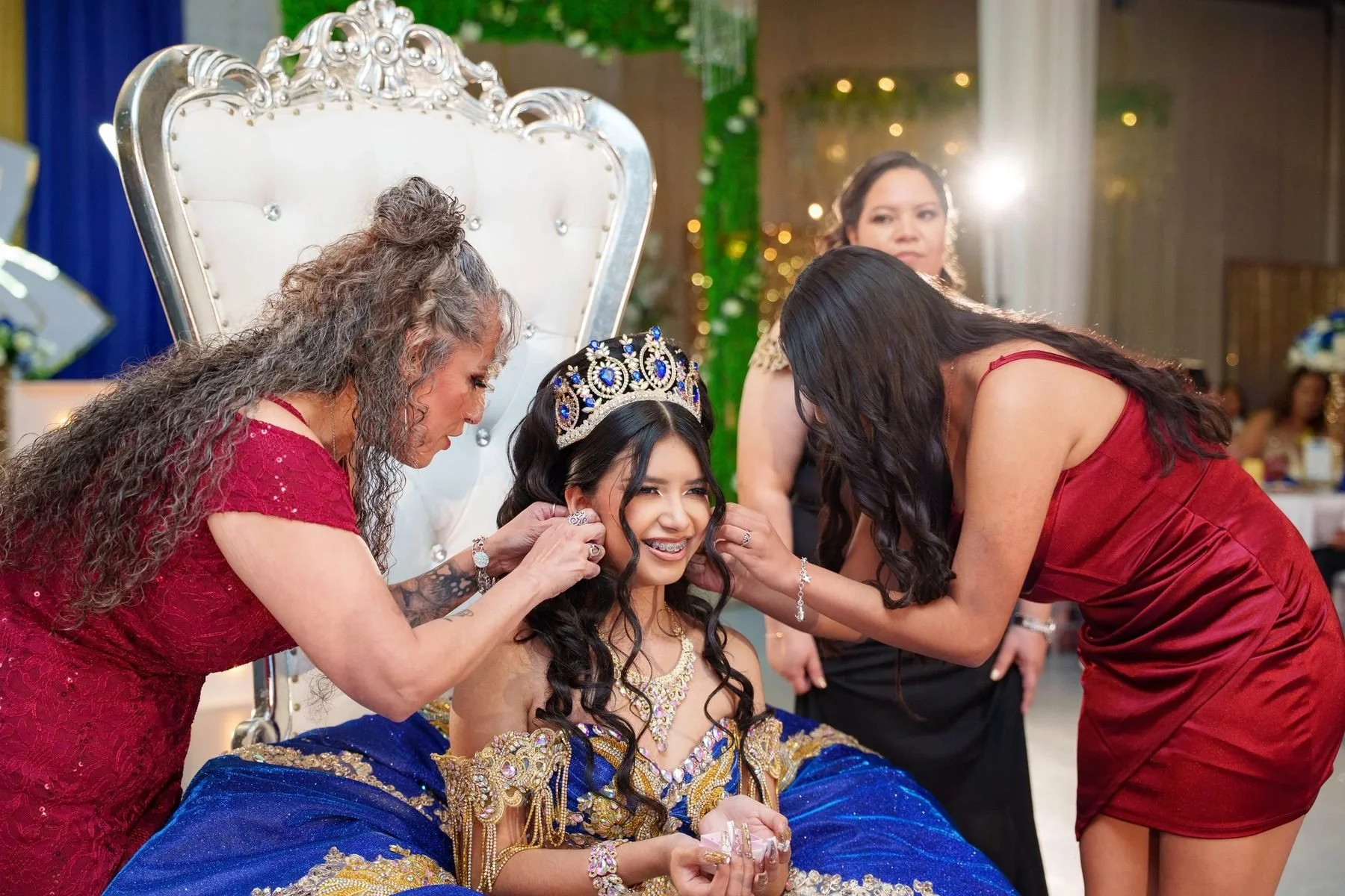 Quinceañera in royal blue gown on her throne as her mom and madrina place her earrings during her DFW celebration