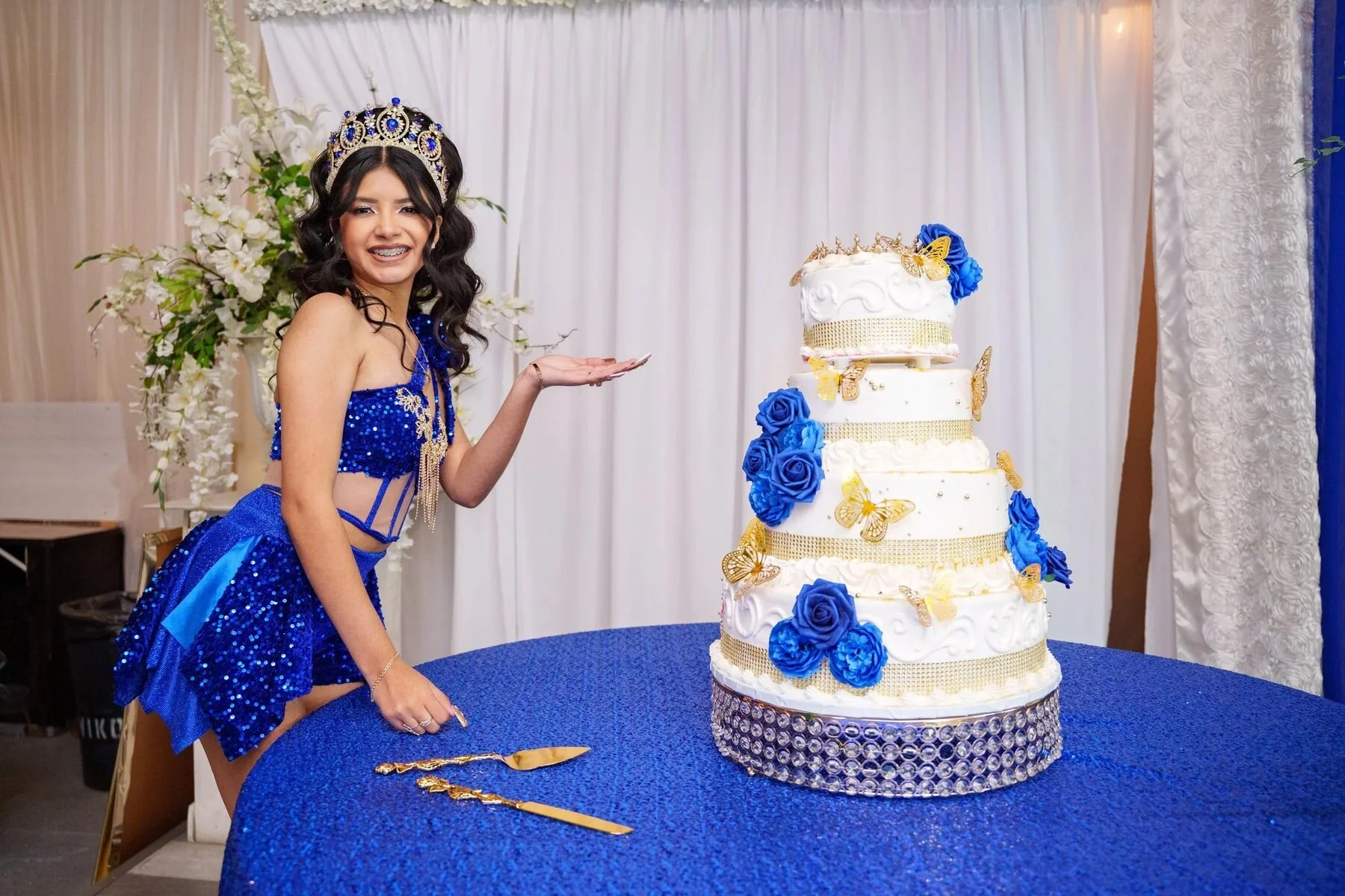 Quinceañera presenting a tall blue and gold tiered cake at a Dallas reception