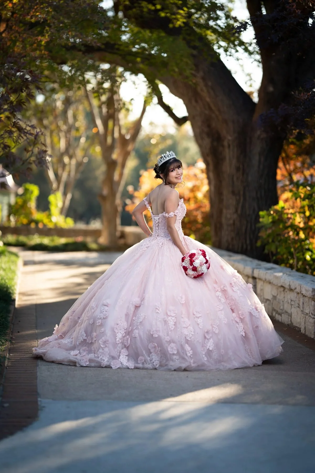 Quinceañera in a blush floral ball gown with a bouquet at a DFW park