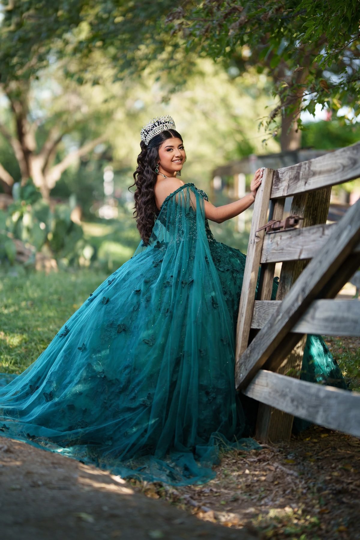 Quinceañera in an emerald western-theme ball gown beside a rustic ranch fence in the Texas countryside.