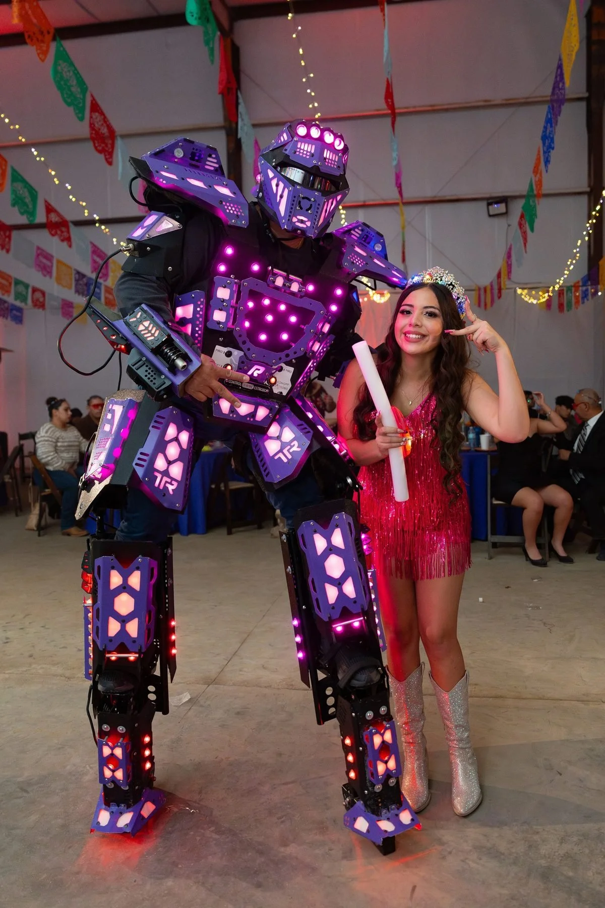 Quinceañera in pink fringe outfit posing with LED robot performer at her after-party in DFW