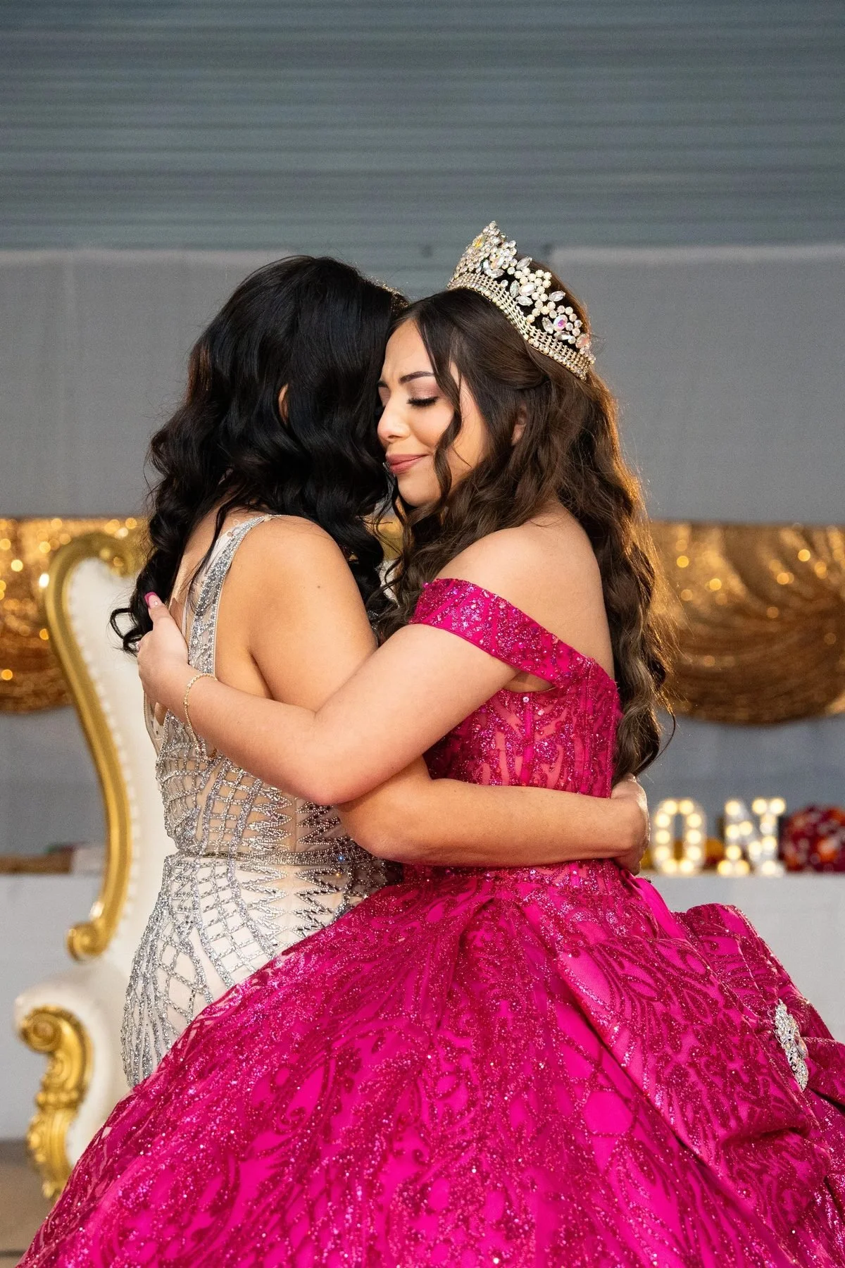 Quinceañera in magenta sparkle gown and gold crown embracing mother in silver gown at Dallas reception