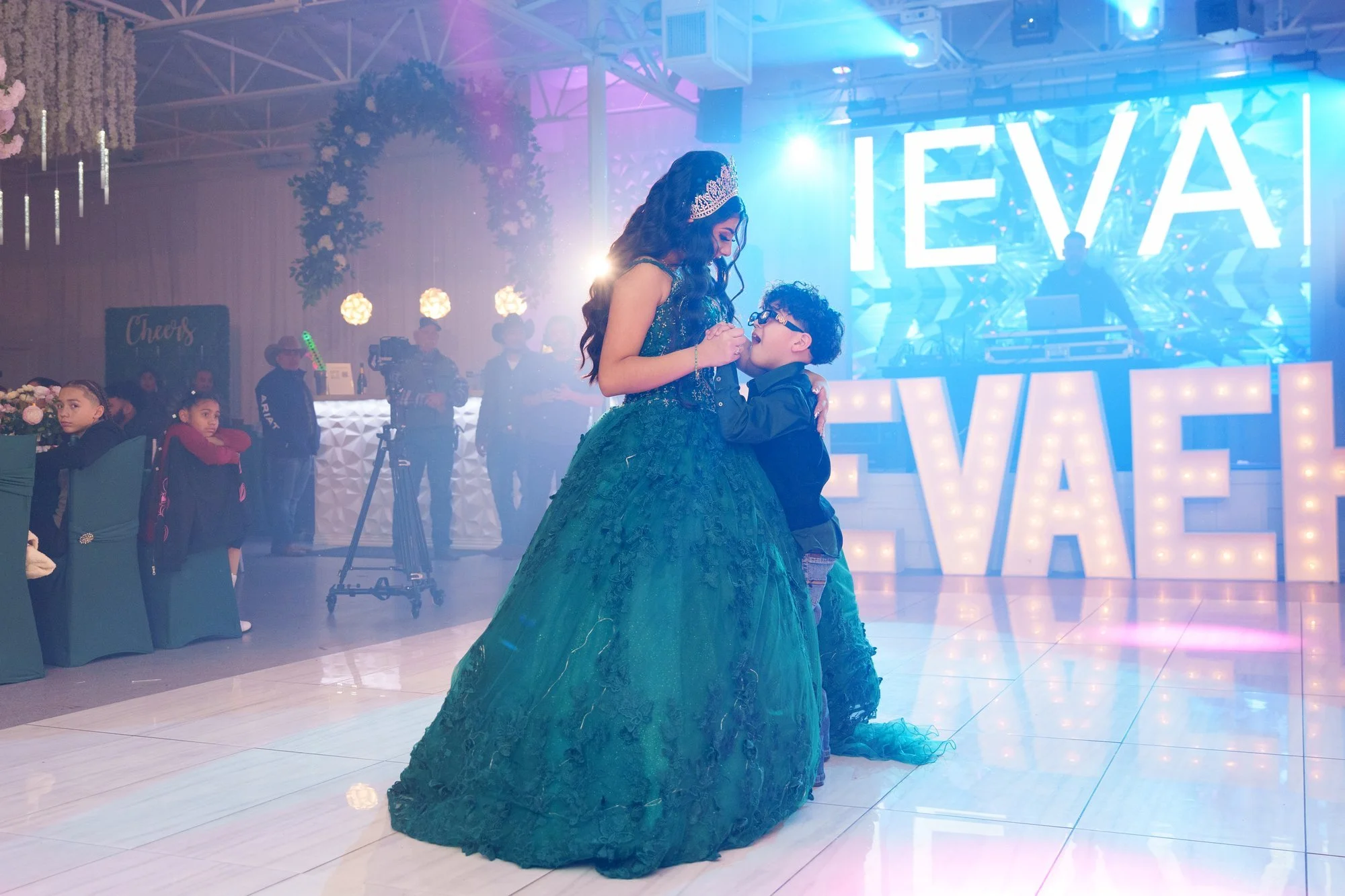 Nevaeh dancing with her little brother in front of the illuminated NEVAEH marquee, tender sibling moment during the reception