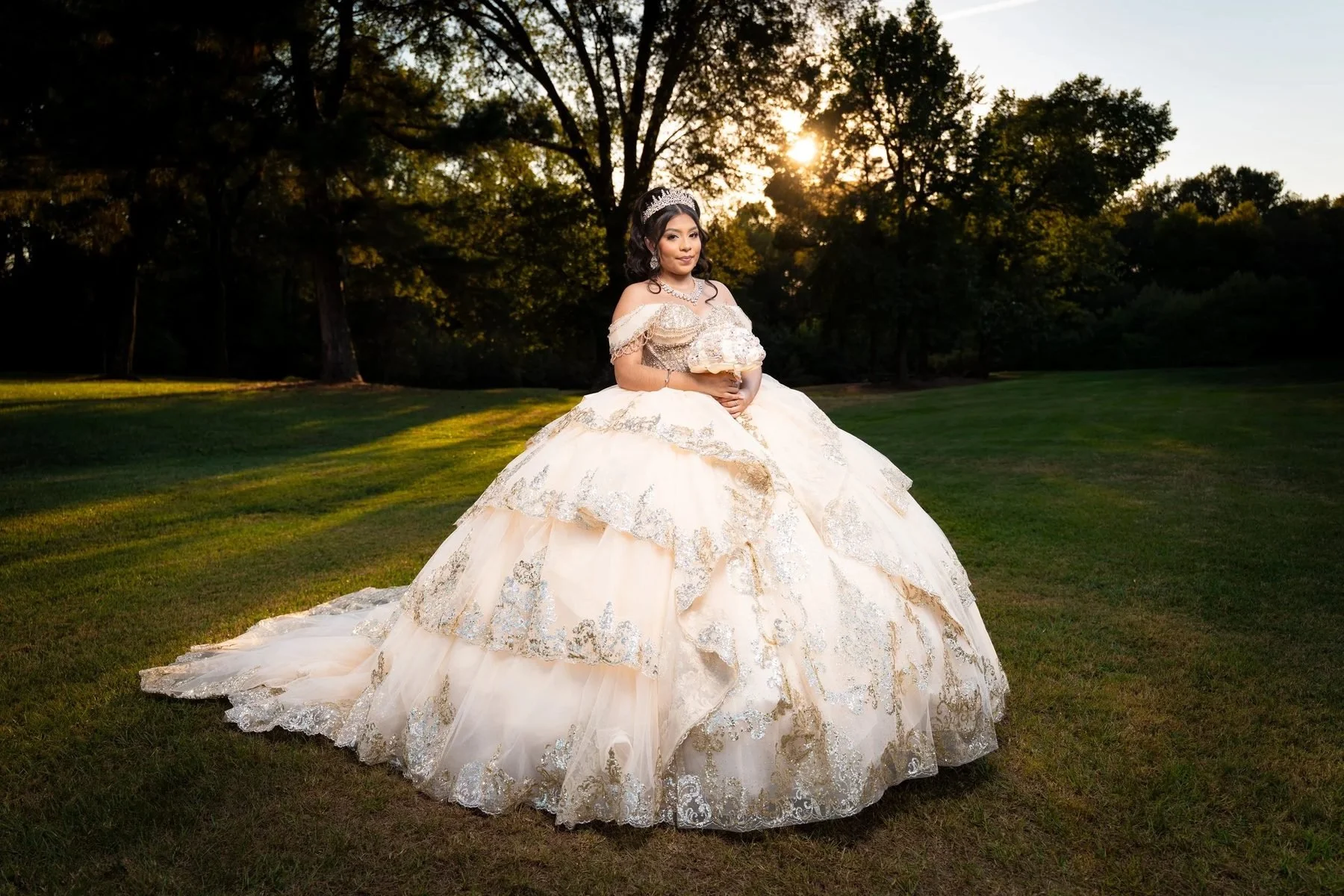 Quinceañera in champagne and gold tiered ball gown holding bouquet in a golden-hour field in DFW