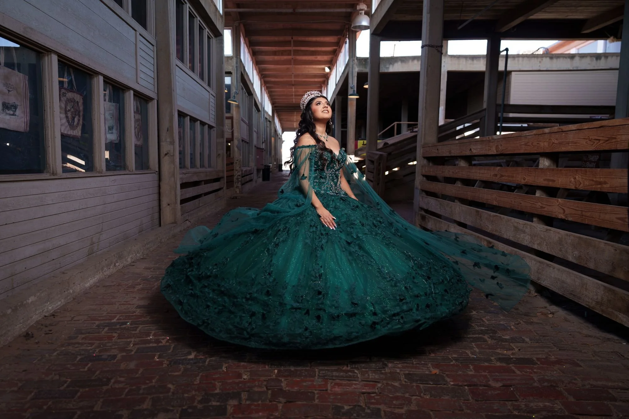 Nevaeh in her emerald ballgown with flared skirt and cape inside the covered cattle pen walkways at Fort Worth Stockyards