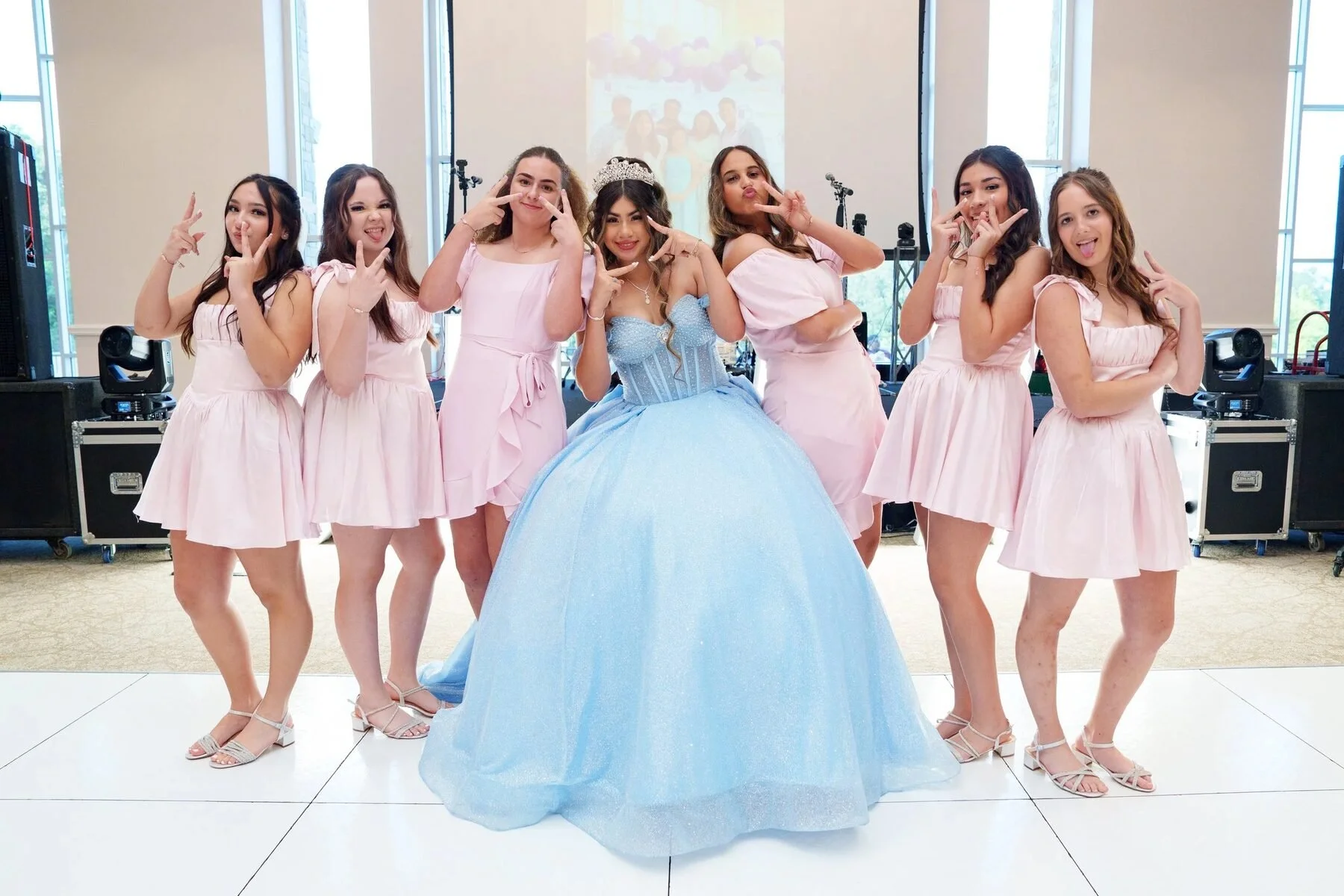 Quinceanera in a blue ballgown laughs with her damas in pink dresses at a Dallas reception.