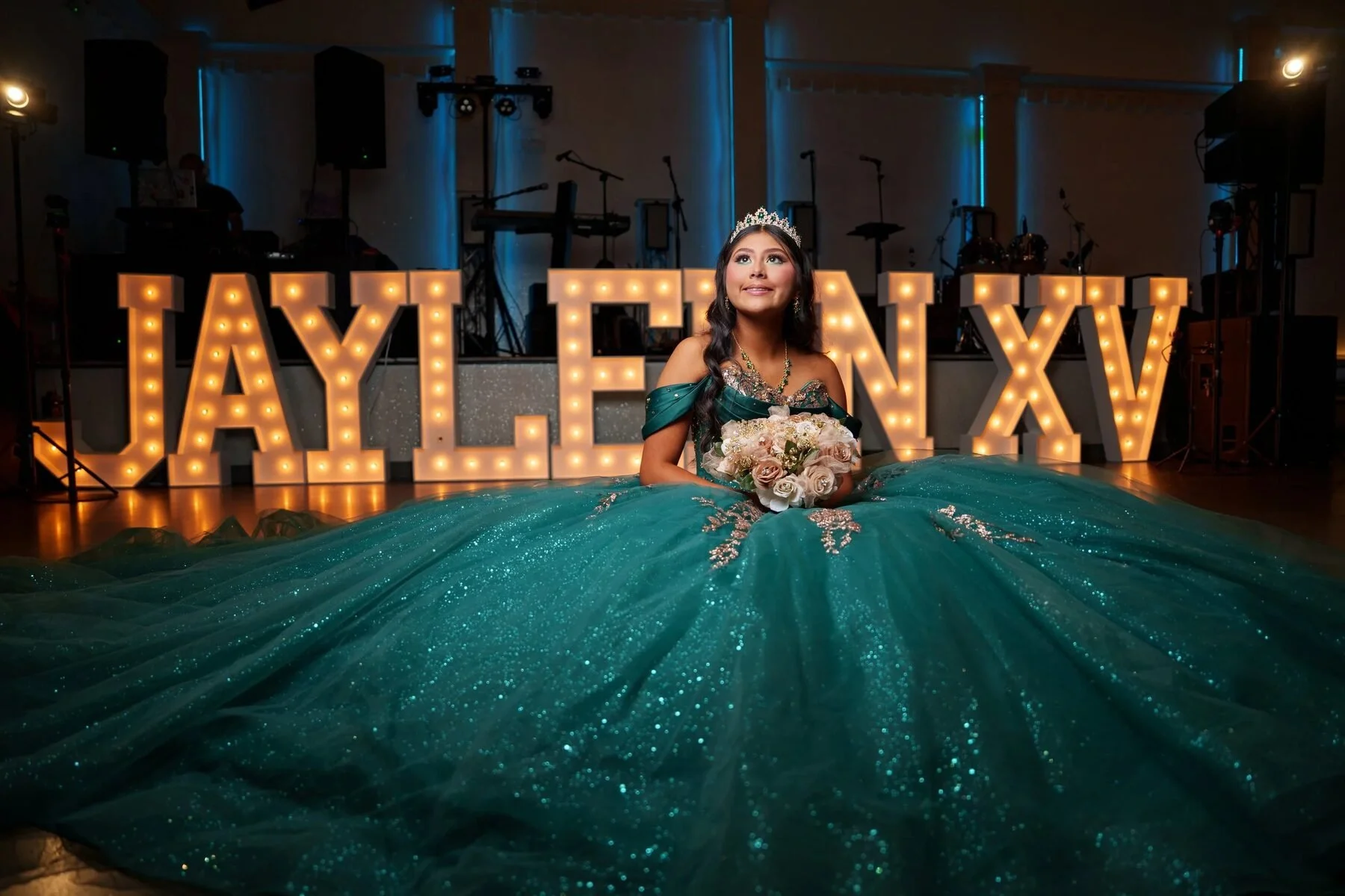 Quinceanera in a teal gown sits before glowing marquee letters at a Fort Worth reception.