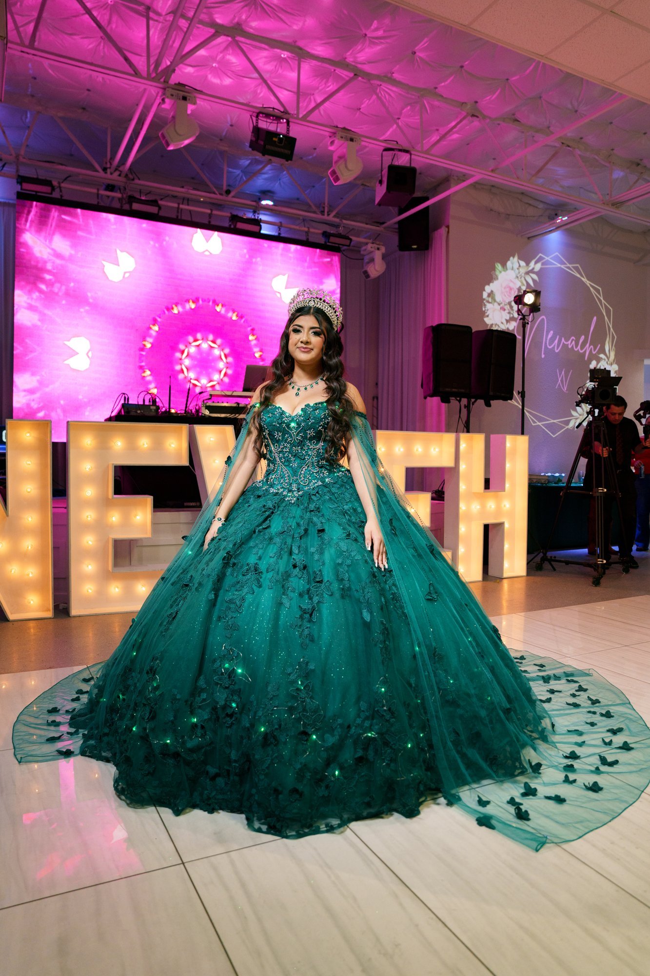 Nevaeh in her emerald quinceañera gown standing in front of illuminated marquee letters spelling her name