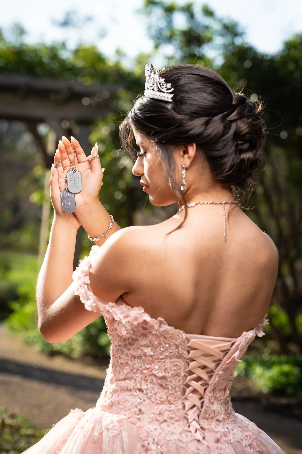 Back view of a quinceañera's blush corset ball gown and tiara in a Dallas garden