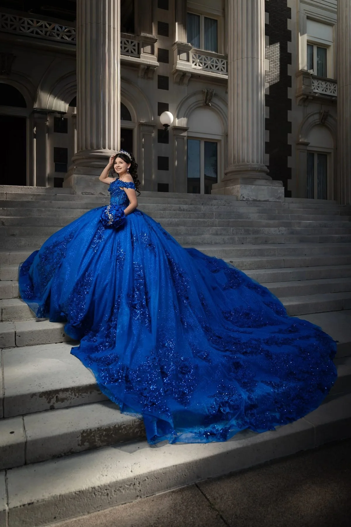 Quinceañera in a royal blue sequined gown with a long train on grand courthouse steps in Dallas.