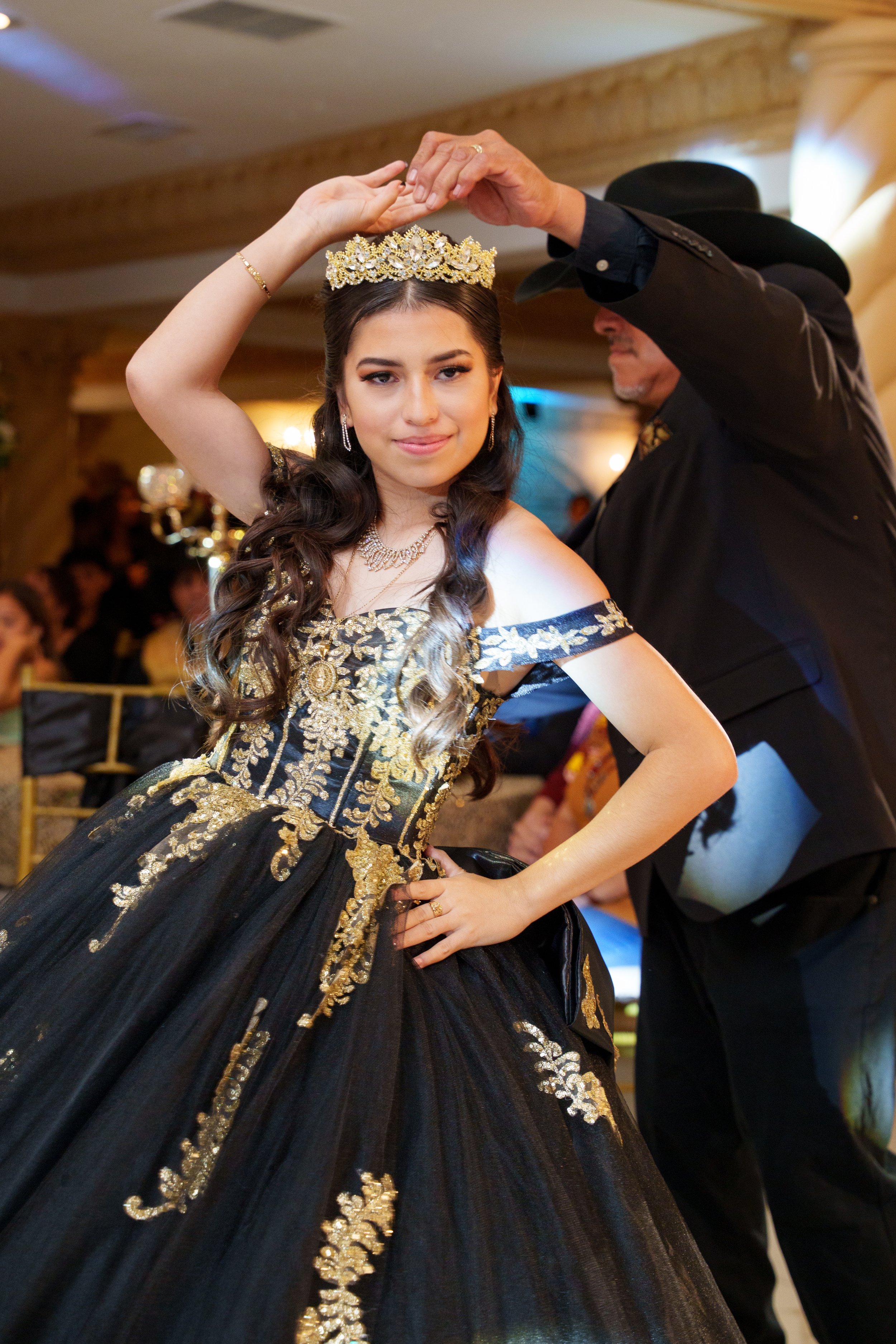 Quinceañera dancing with her father during the father daughter dance, wearing a black and gold quince dress and crown at her quinceañera reception.