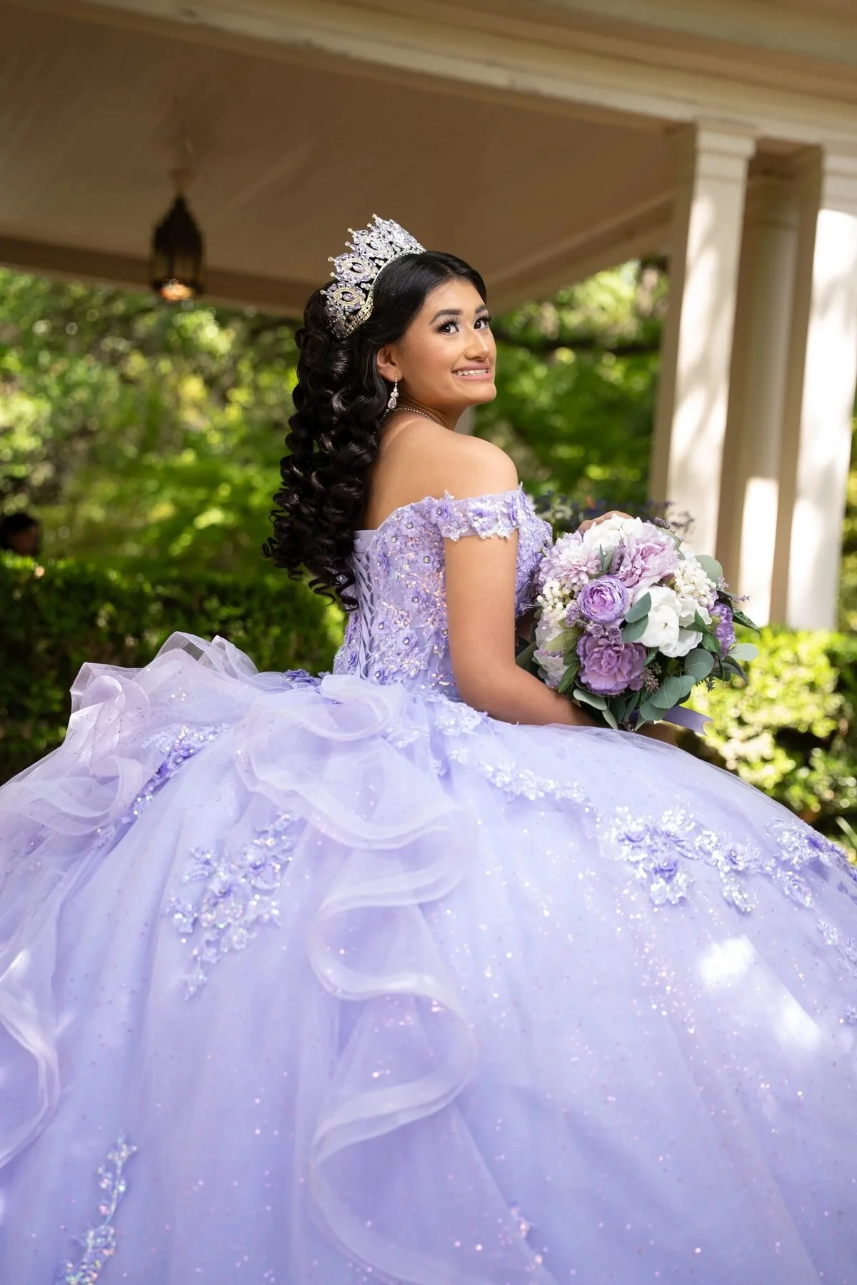 Quinceañera in a lavender ruffled gown holding a bouquet in a Dallas garden gazebo