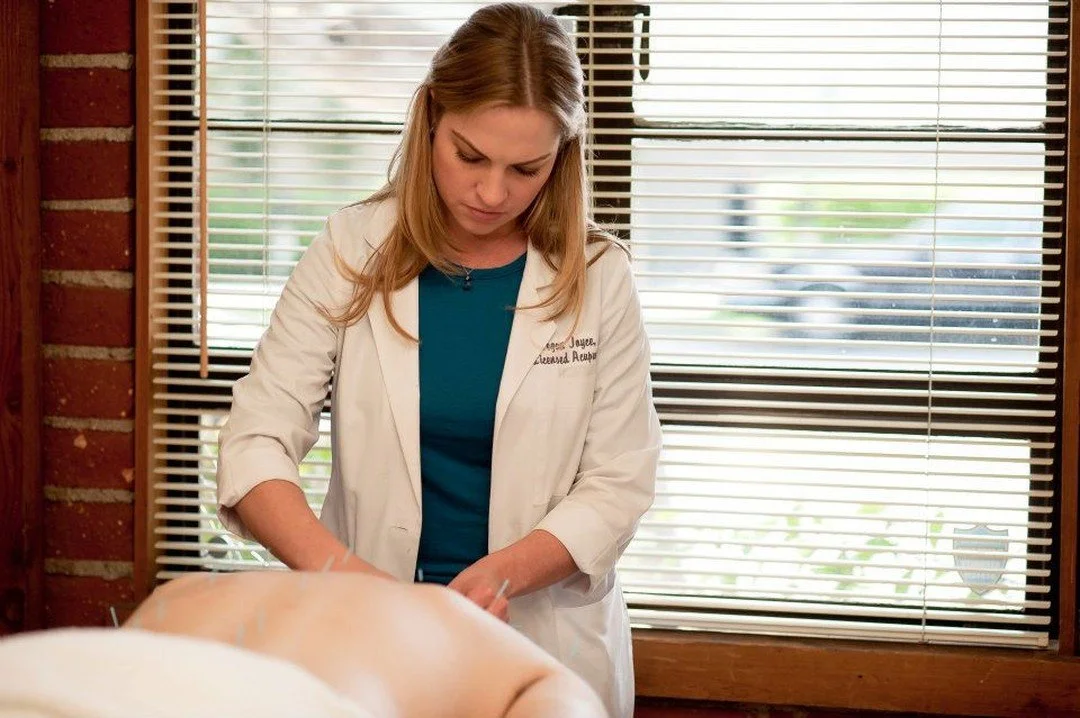 Megan Joyce, LAc FABORM in a white coat providing acupuncture treatment on a patient lying face down.
