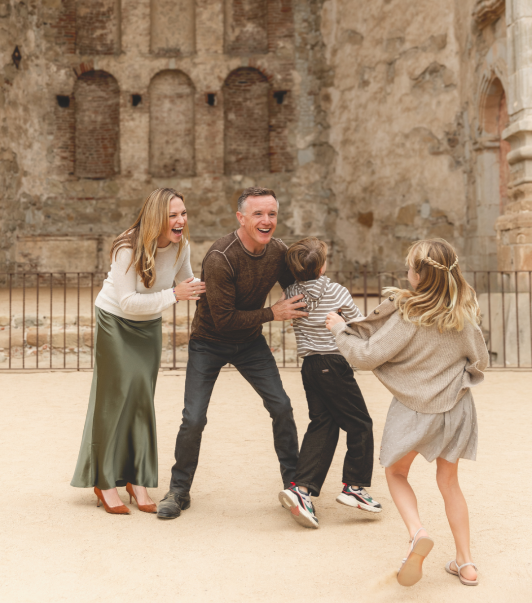 Family playing and laughing outdoors in front of an ancient stone wall.