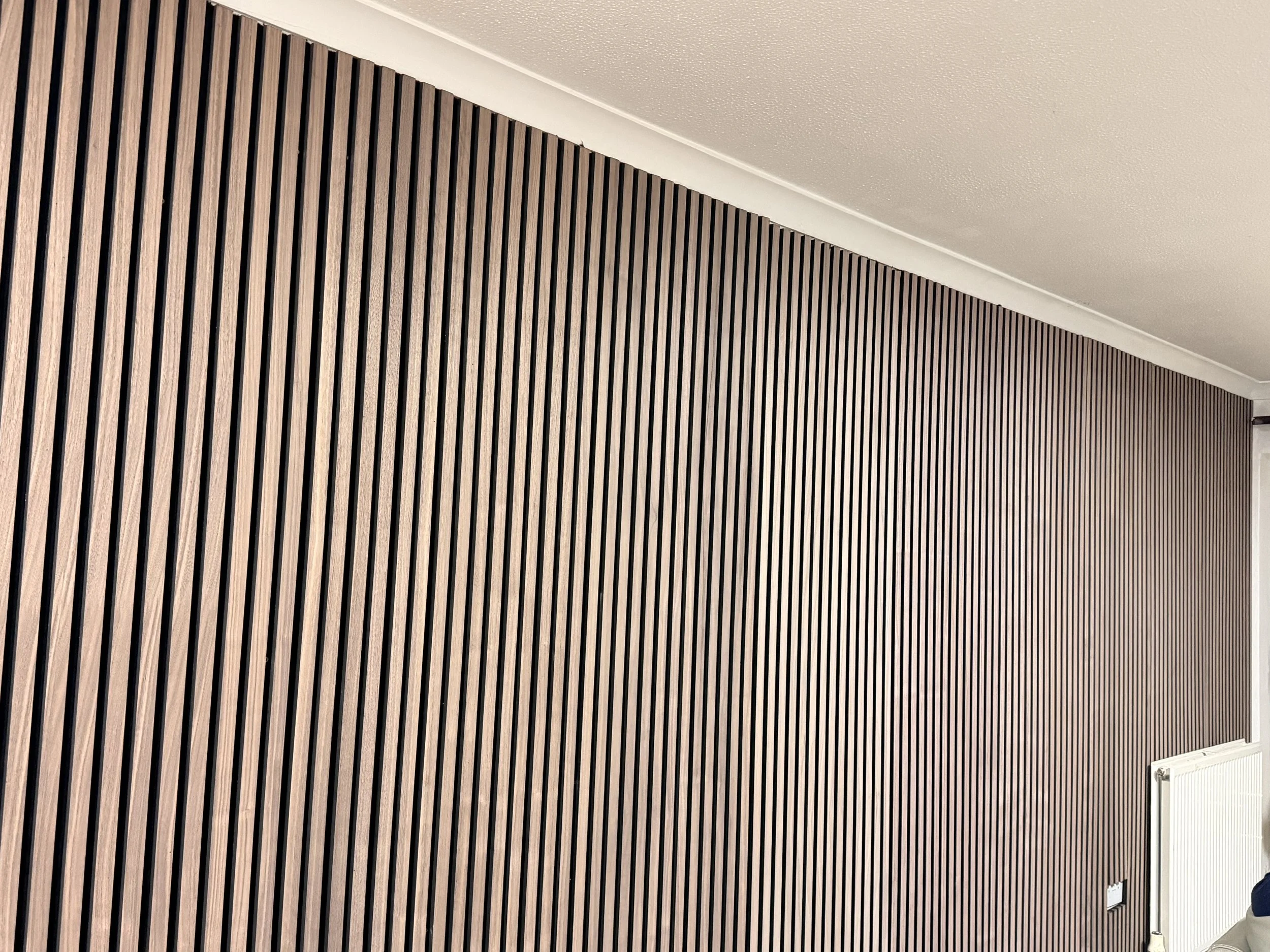 Interior wall with vertical wooden slats and a radiator near the floor.