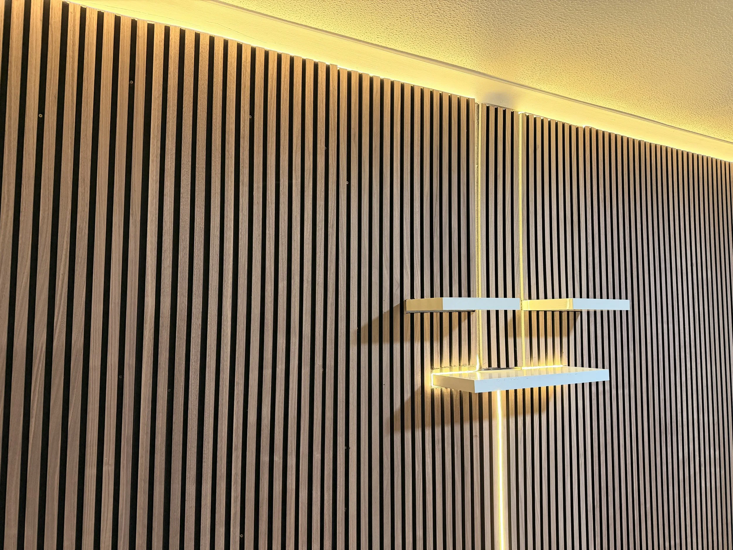 A modern interior wall decor with vertical wooden slats and a floating shelf illuminated by yellow LED lights.