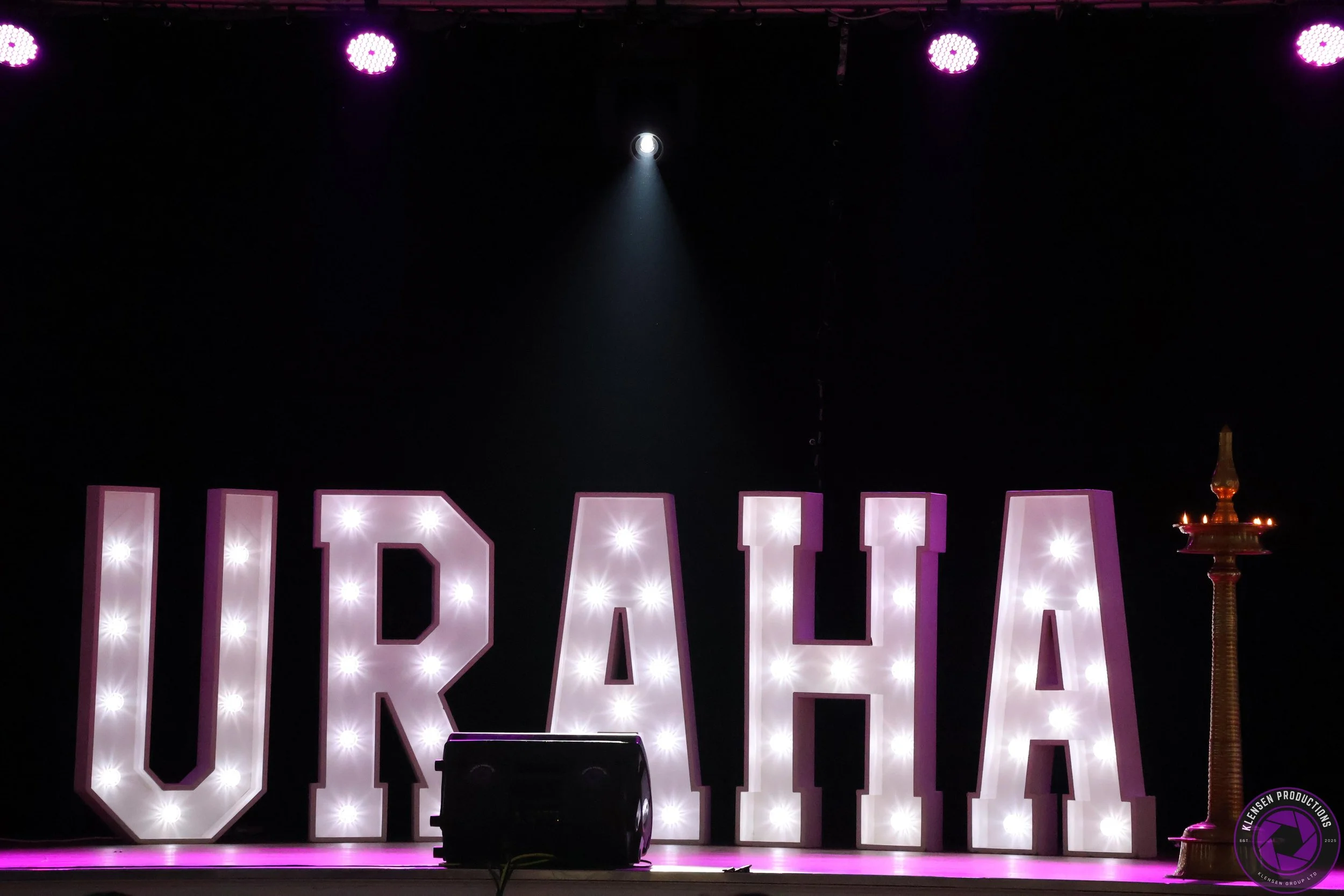 Stage with large illuminated letters spelling Vermont, purple lighting, and a traditional Vermont maple syrup dispenser on the right.