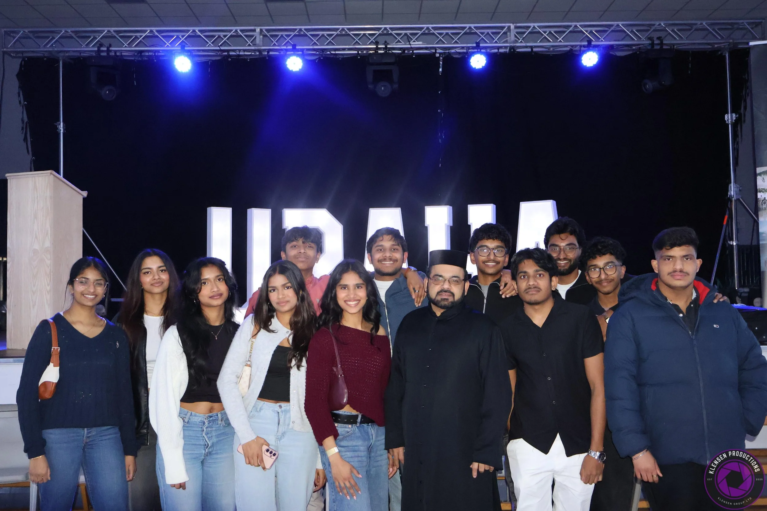 Group of people standing on stage in front of illuminated sign that reads 'UCAF'.