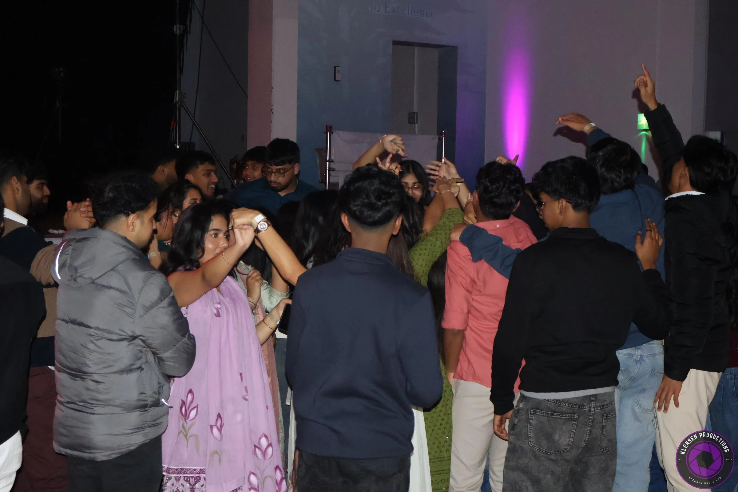 Group of young people dancing and socializing at a lively indoor event with colorful lighting.