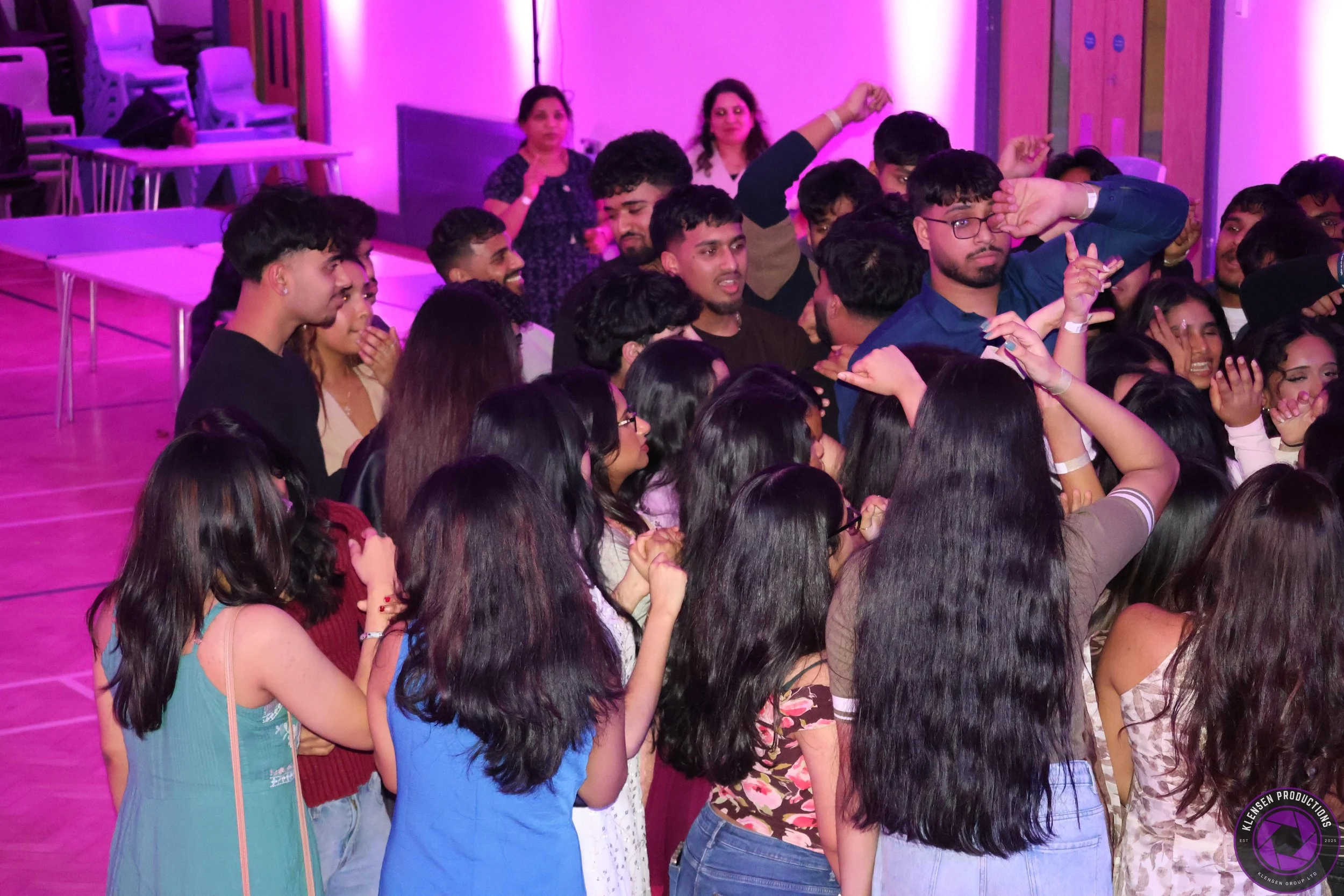 A group of young people dancing and having fun in a room with pink and purple lighting.