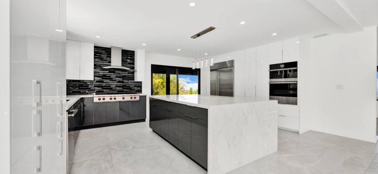 Wide view of a kitchen with a light stone waterfall island, white cabinets and dark backsplash