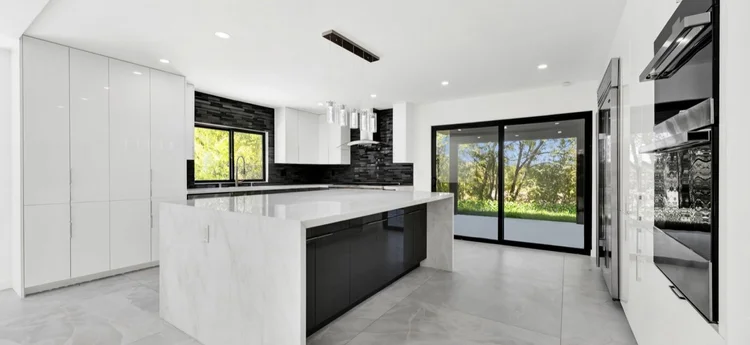 Modern kitchen with white cabinetry, black accents, a large marble island, and sliding glass doors leading outside.
