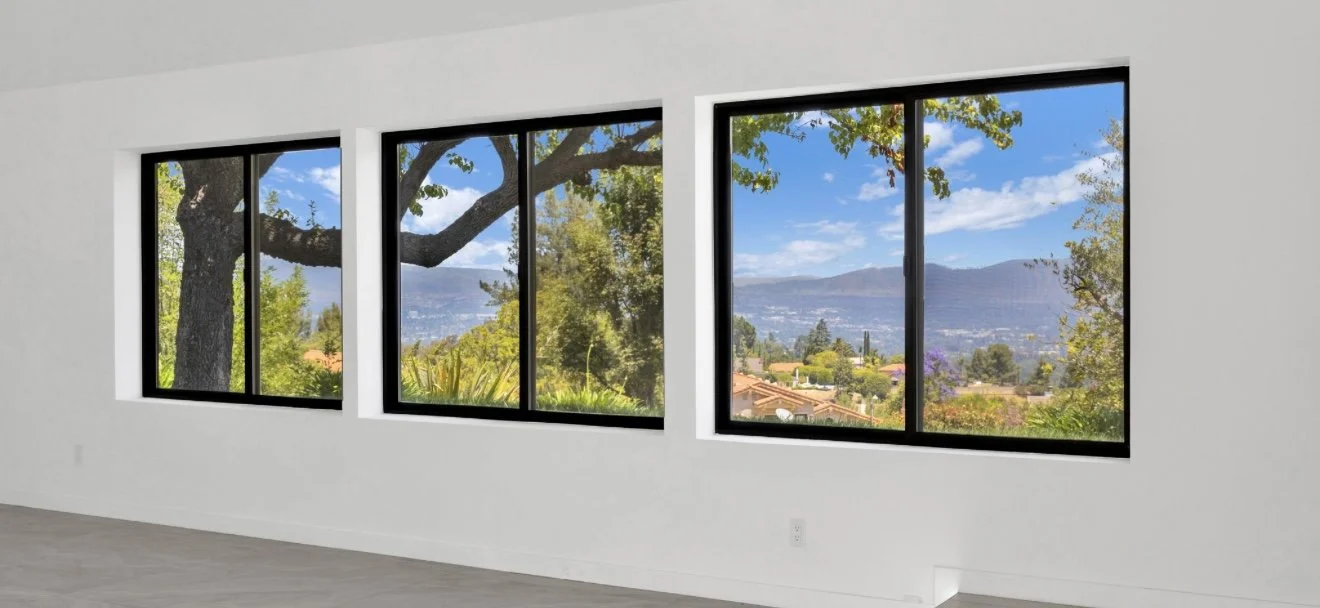 Bright interior room with wood flooring and three dark-framed windows.
