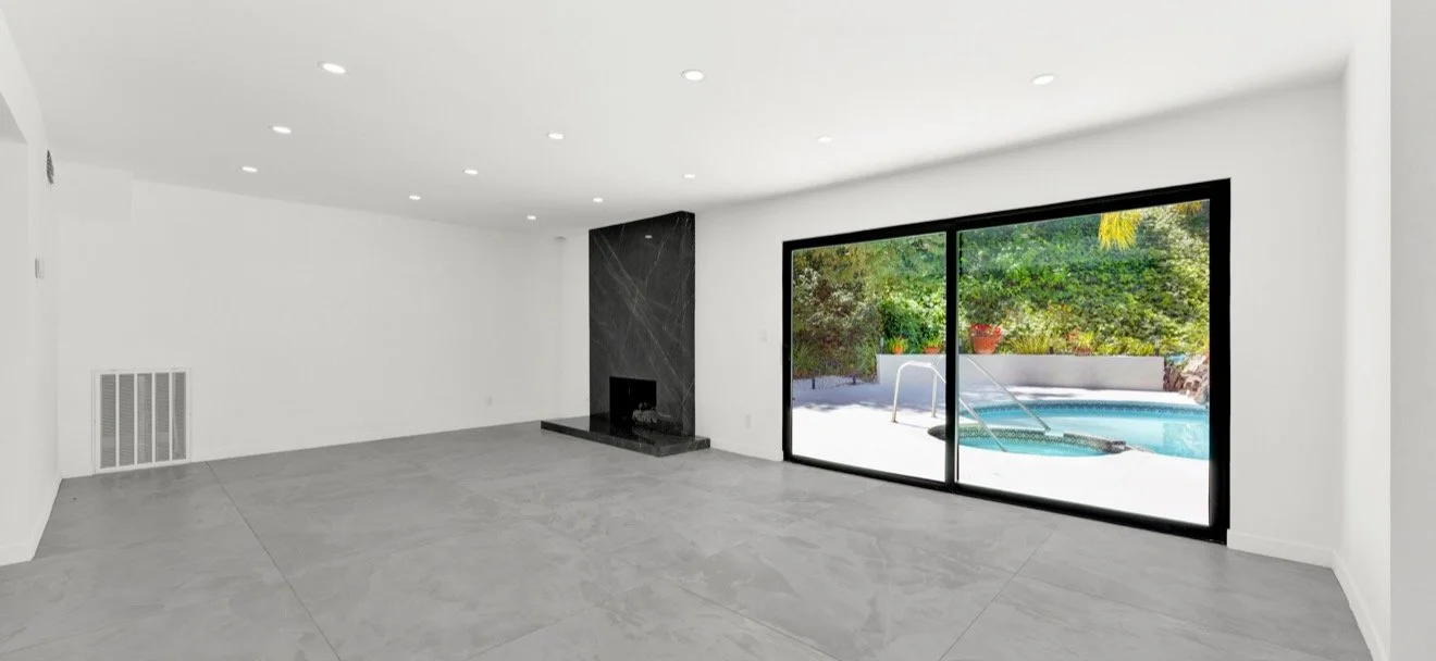 Bright living room with a dark fireplace and black-framed sliding doors opening toward a pool