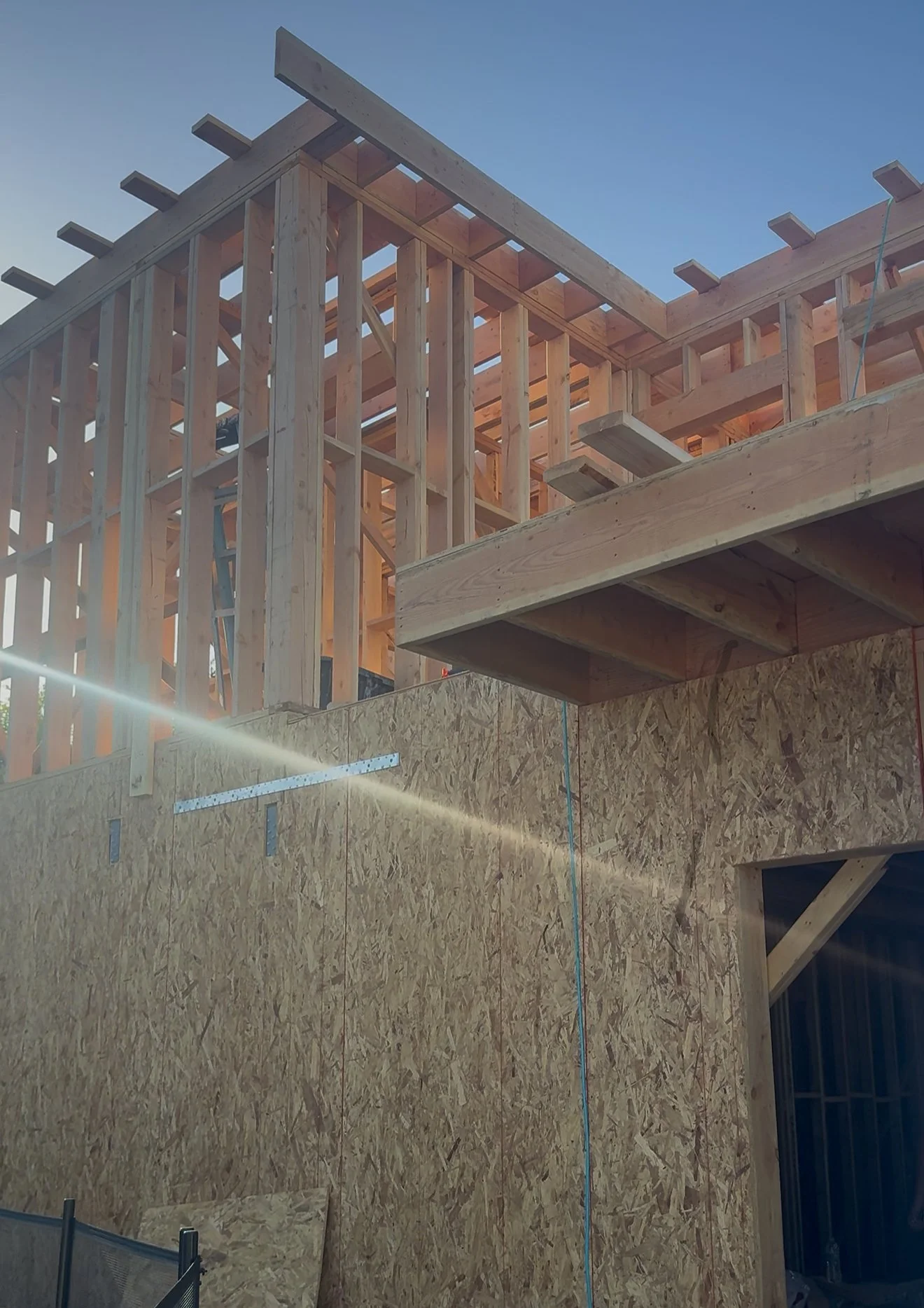 Wood framing and plywood walls at a construction site beneath a blue sky.