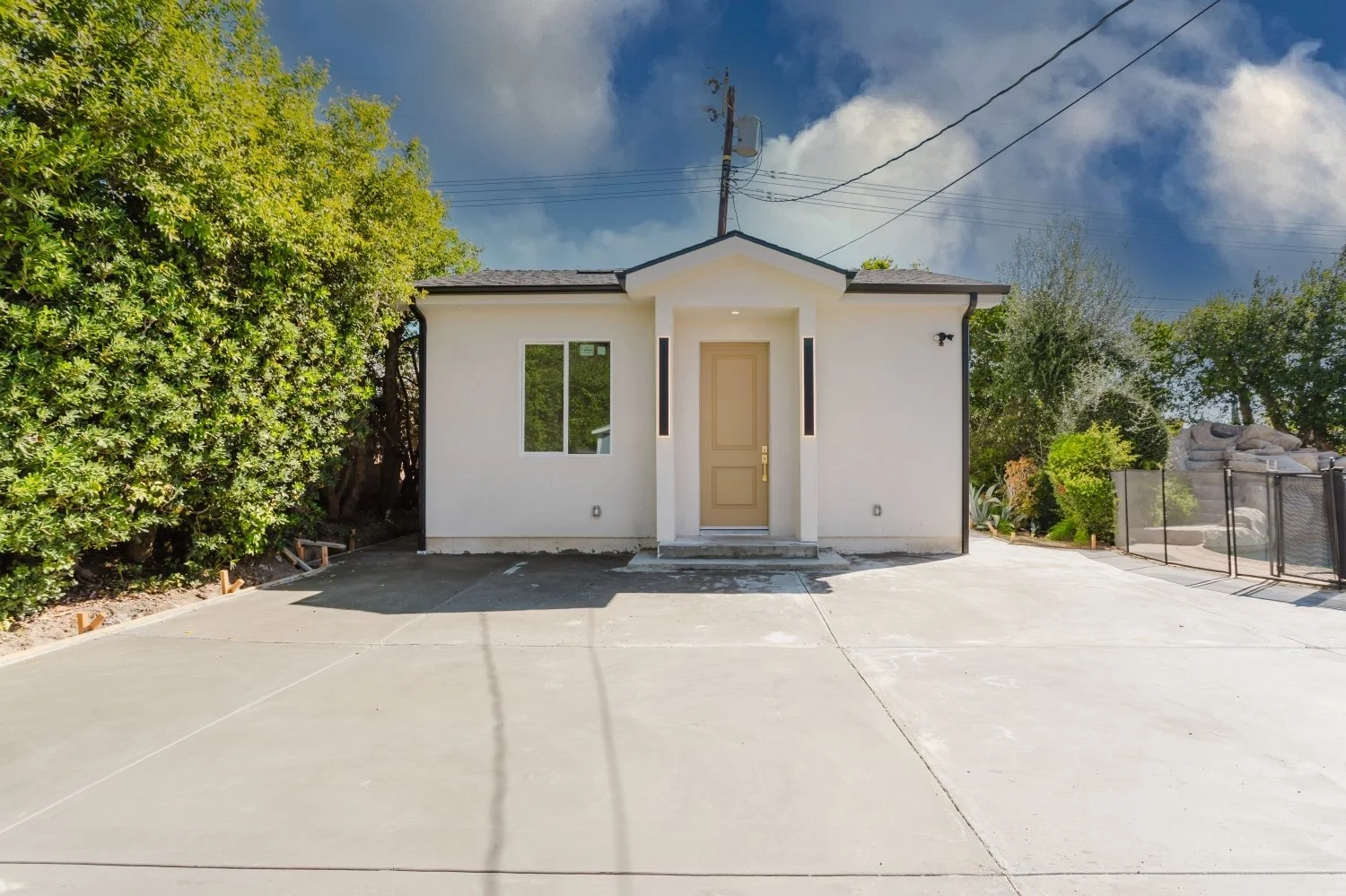 Exterior of a small white building with a beige front door, dark-framed windows and a paved entry.